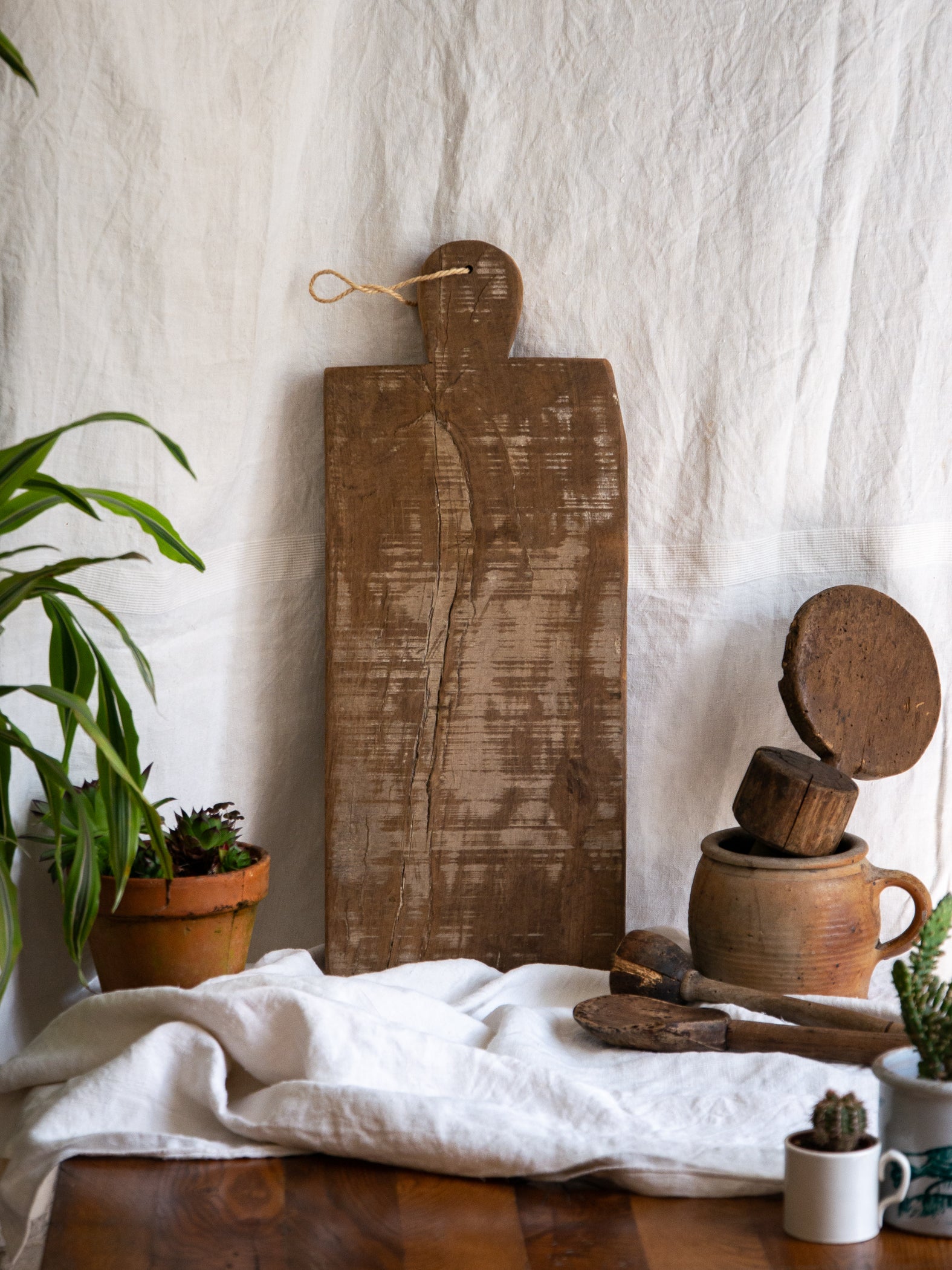 A large vintage wooden chopping board from south west France, shaped by years of use and hand-worn edges. Its rough texture and deep patina tell the story of daily bread, shared meals, and time well lived.