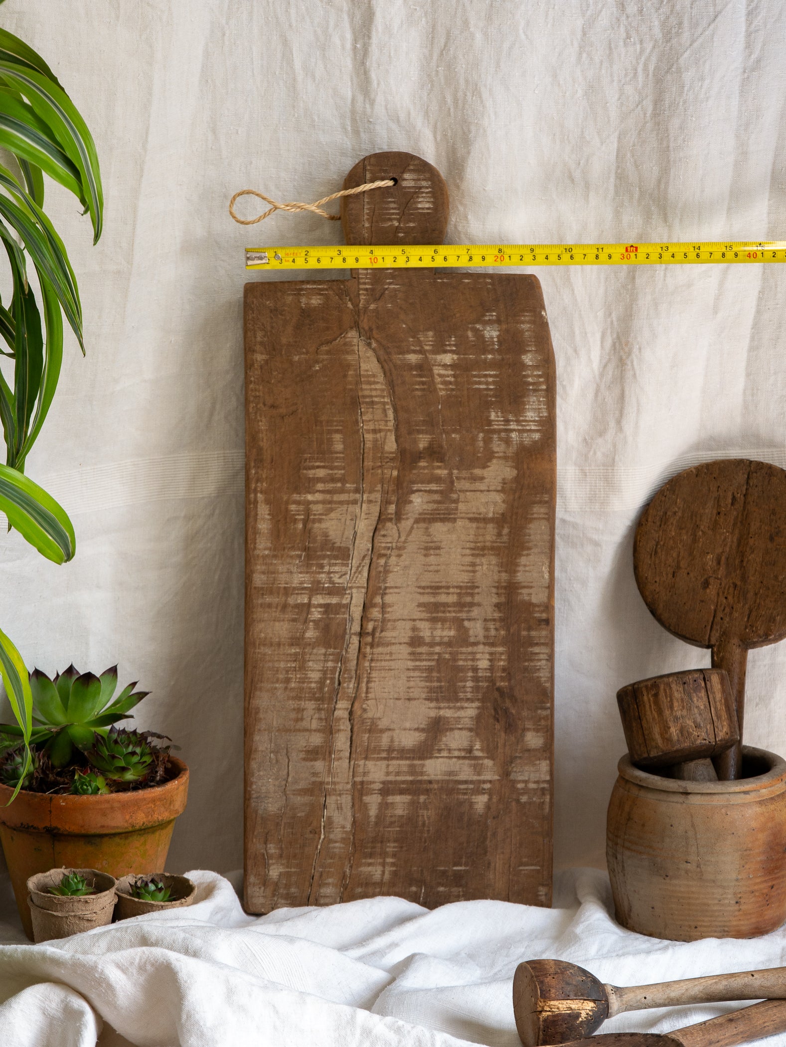 A large vintage wooden chopping board from south west France, shaped by years of use and hand-worn edges. Its rough texture and deep patina tell the story of daily bread, shared meals, and time well lived.