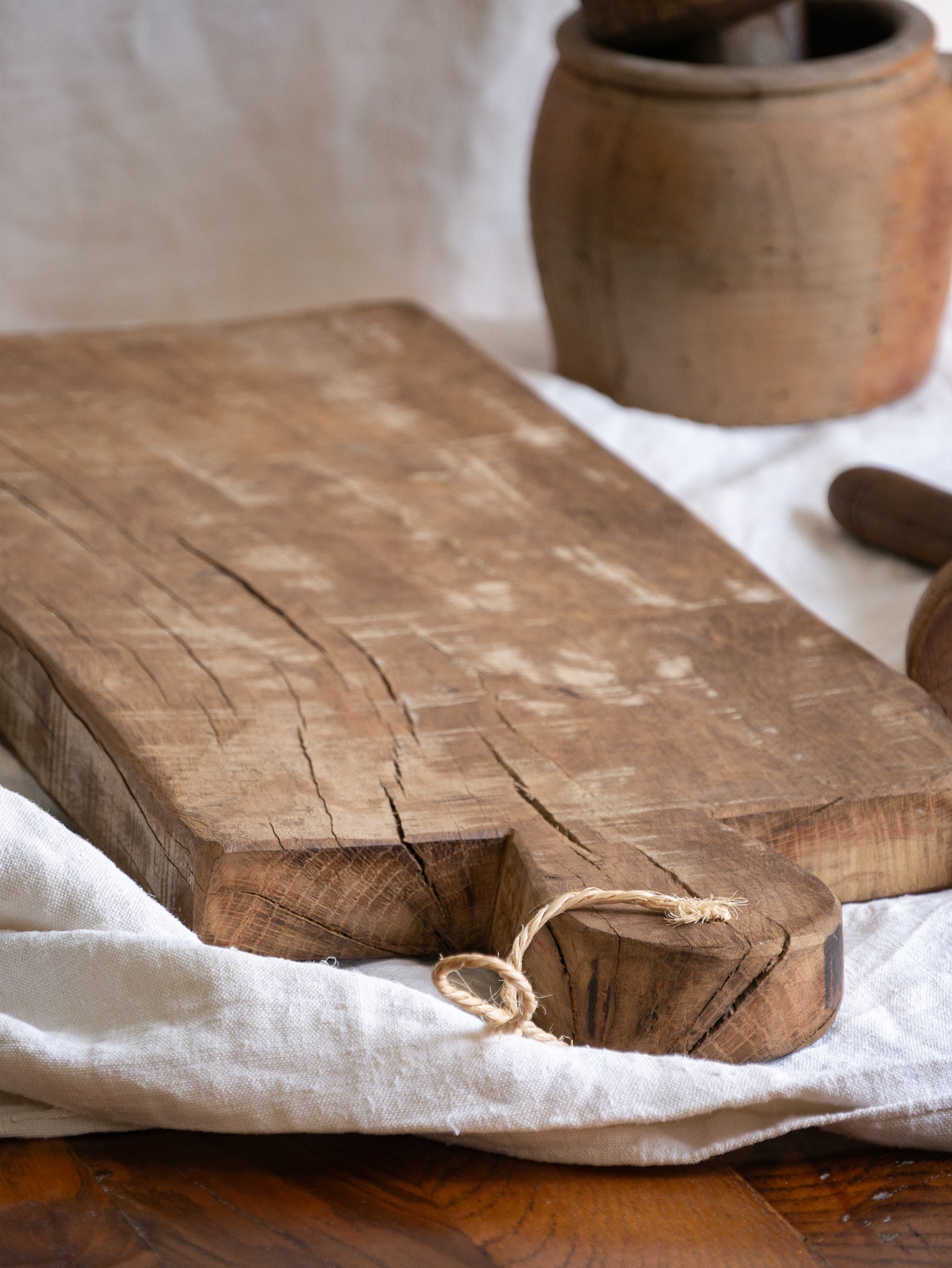 A large vintage wooden chopping board from south west France, shaped by years of use and hand-worn edges. Its rough texture and deep patina tell the story of daily bread, shared meals, and time well lived.