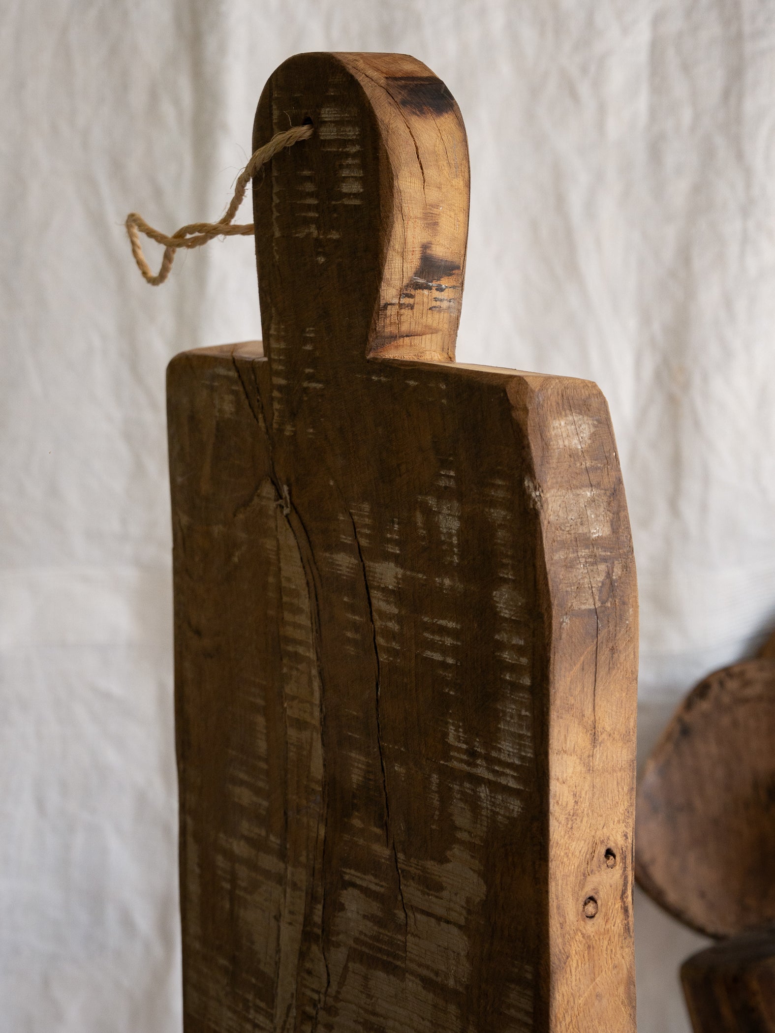 A large vintage wooden chopping board from south west France, shaped by years of use and hand-worn edges. Its rough texture and deep patina tell the story of daily bread, shared meals, and time well lived.