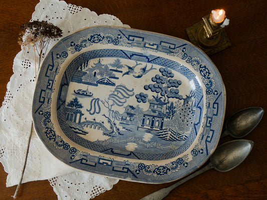 Blue and white patterned plate on a wooden surface with a candle and silverware.