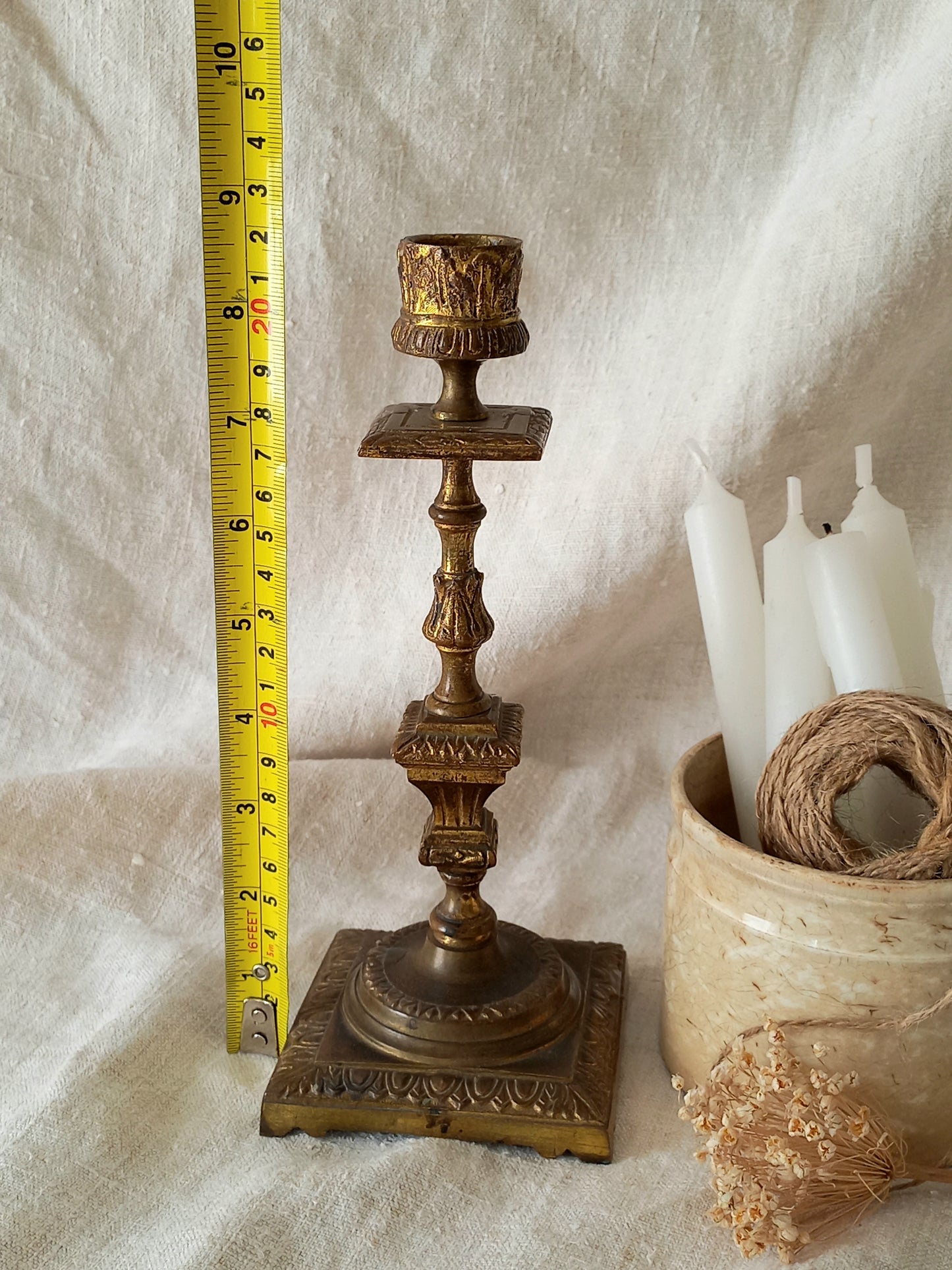 Decorative brass candlestick with a measuring tape on a textured white background