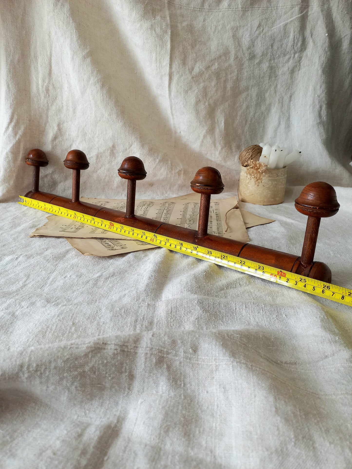 Wooden coat rack with five hooks on a textured white fabric background and a tape measure for reference.