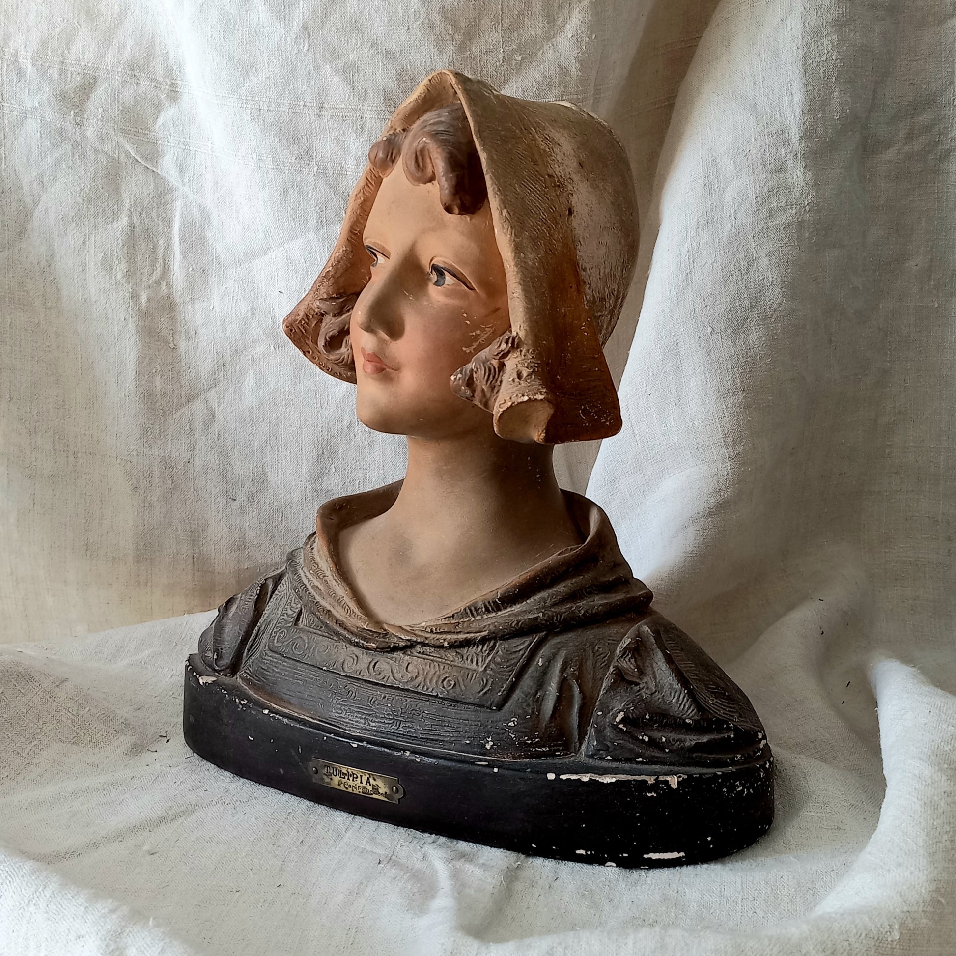 Antique bust of a woman wearing a bonnet on a white fabric background