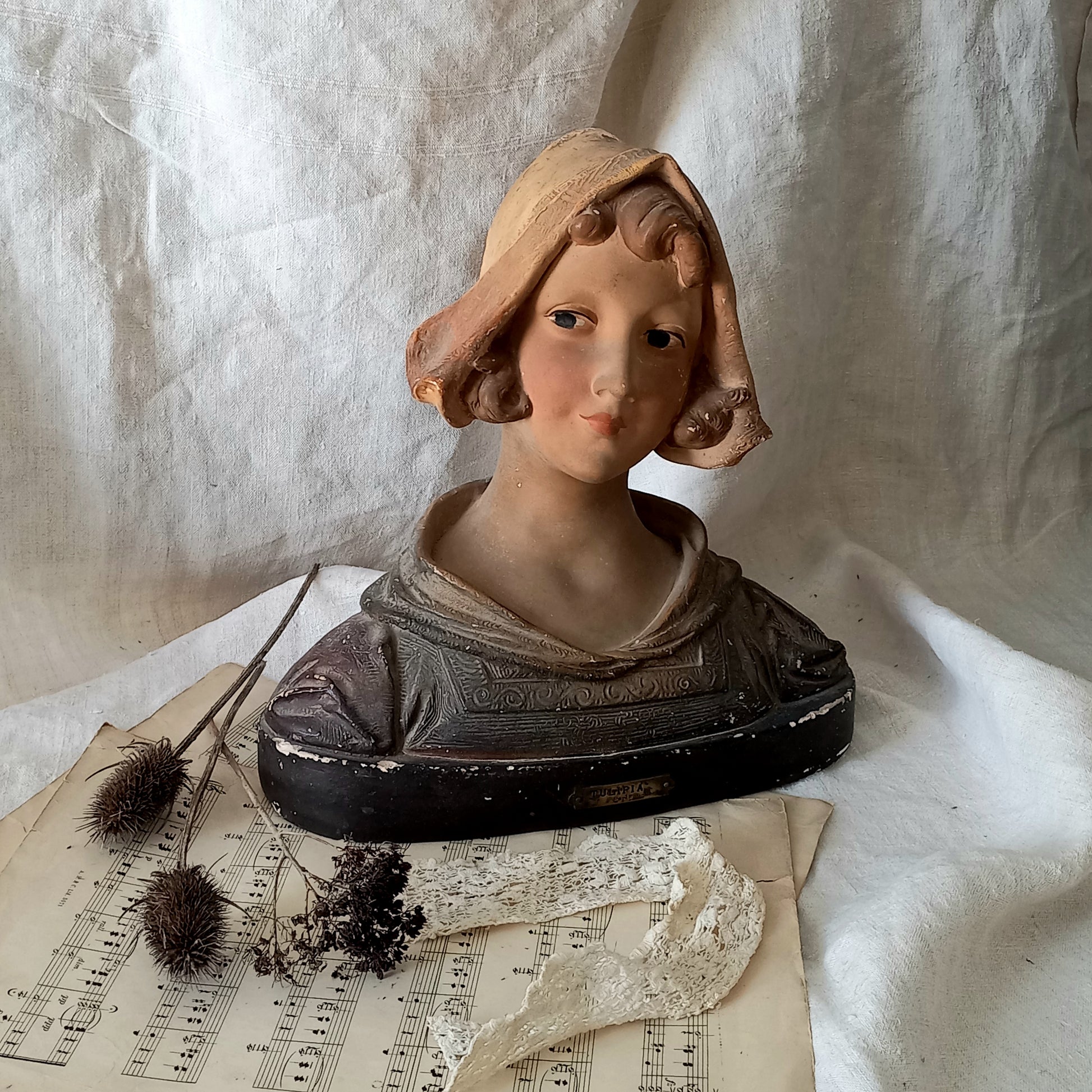 Antique bust of a woman wearing a bonnet on a white fabric background
