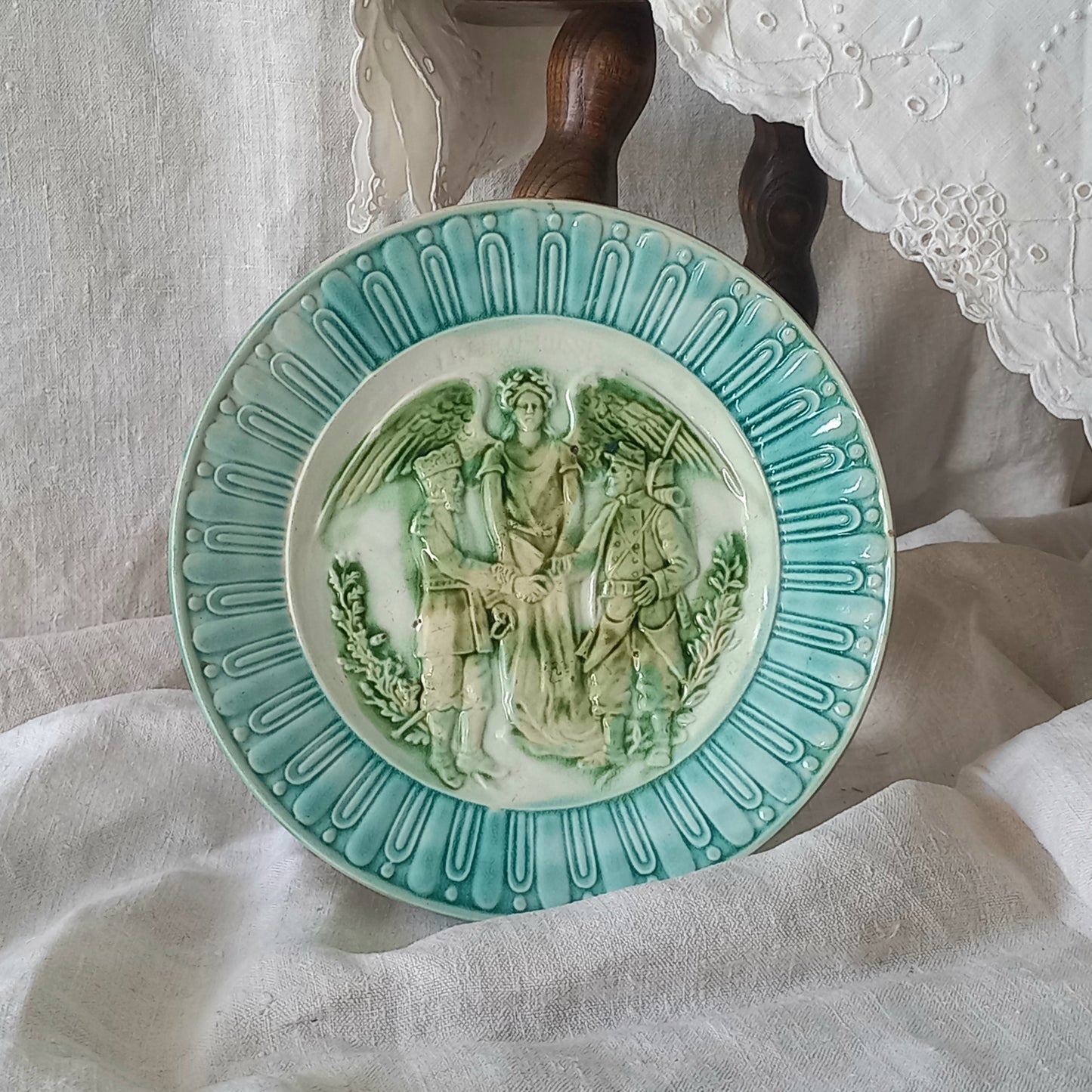 A French antique decorative majolica plate with stunning blue/green colours and an interesting historical background.
This lovely old plate was manufactured as a commemorative piece to celebrate the Franco-Russian Alliance made by the French Republic and the Russian Empire between 1891-1894 (military co-operation agreements) – and that lasted until 1917. The plate depicts a Russian and French soldier shaking hands with a winged female angel in between them.