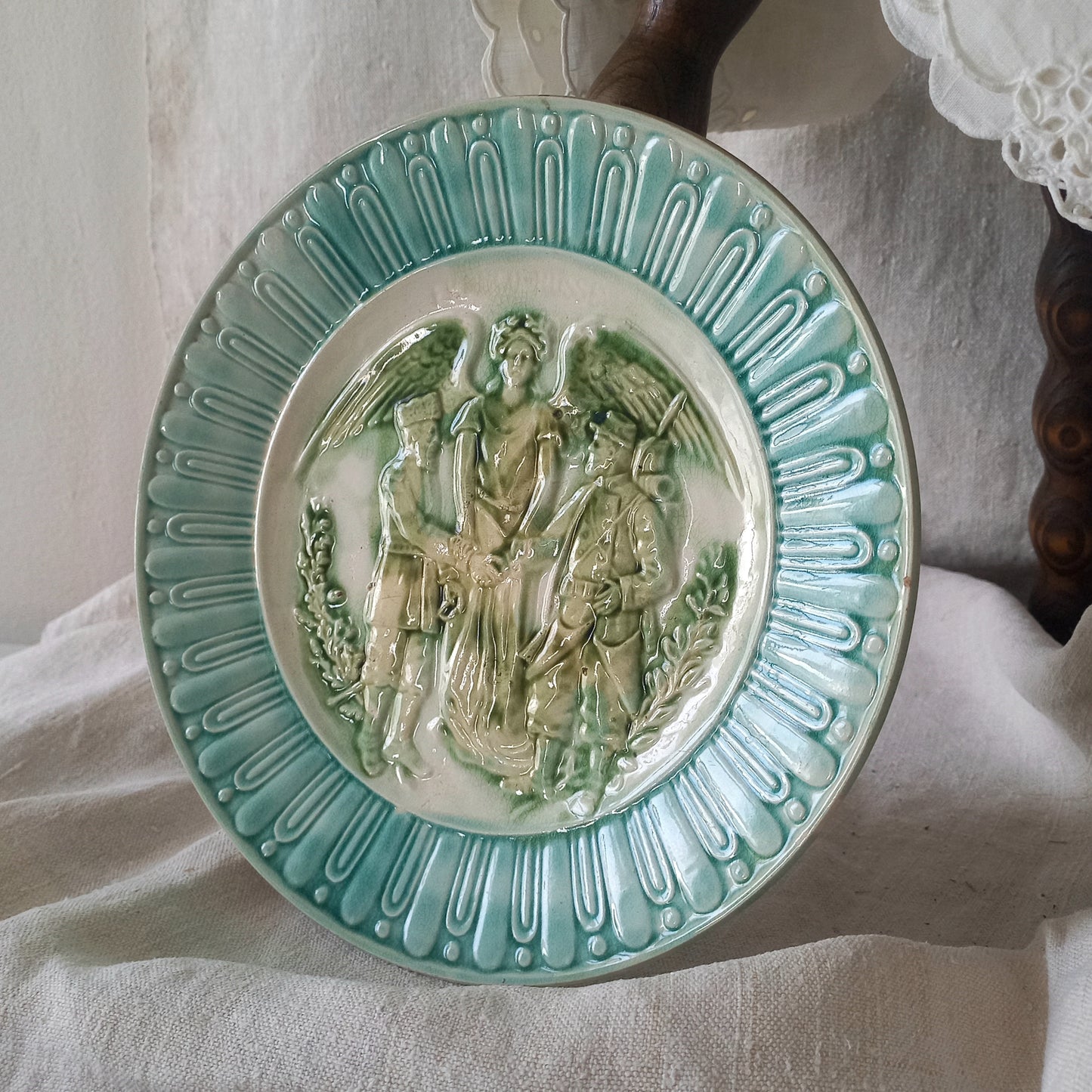 A French antique decorative majolica plate with stunning blue/green colours and an interesting historical background.
This lovely old plate was manufactured as a commemorative piece to celebrate the Franco-Russian Alliance made by the French Republic and the Russian Empire between 1891-1894 (military co-operation agreements) – and that lasted until 1917. The plate depicts a Russian and French soldier shaking hands with a winged female angel in between them.