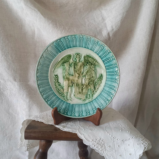 A French antique decorative majolica plate with stunning blue/green colours and an interesting historical background.
This lovely old plate was manufactured as a commemorative piece to celebrate the Franco-Russian Alliance made by the French Republic and the Russian Empire between 1891-1894 (military co-operation agreements) – and that lasted until 1917. The plate depicts a Russian and French soldier shaking hands with a winged female angel in between them.
