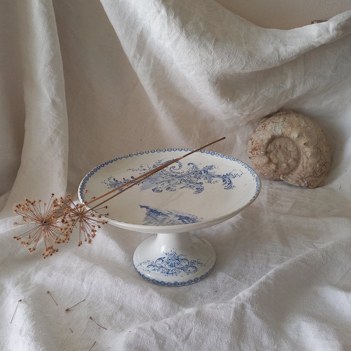 An attractive French antique footed ironstone cake plate with a blue transfer pattern depicting architecture, cherubs, and flowers; a very pretty and delicate pattern.
Original antique ironstone pieces of this age and condition are becoming increasingly difficult to source to this a rare treat to discover.