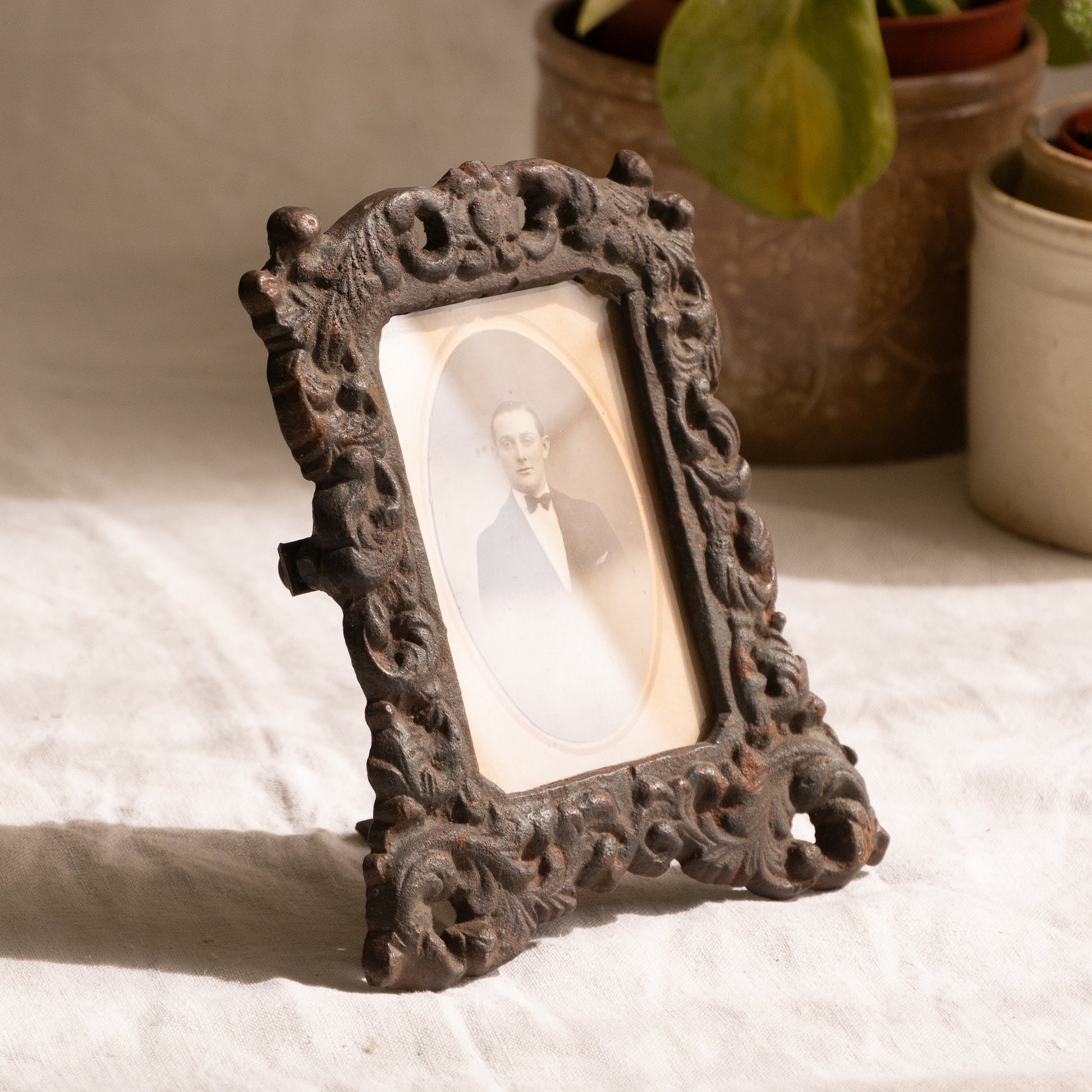 A small French antique decorative cast iron photo frame - a very interesting artisan-made table-top frame with wonderful time-worn patina. There is a glass front and a hardboard backing board. The photo of the gentleman in a tuxedo is an original French period photo that we have placed inside for display purposes and is included in the sale.