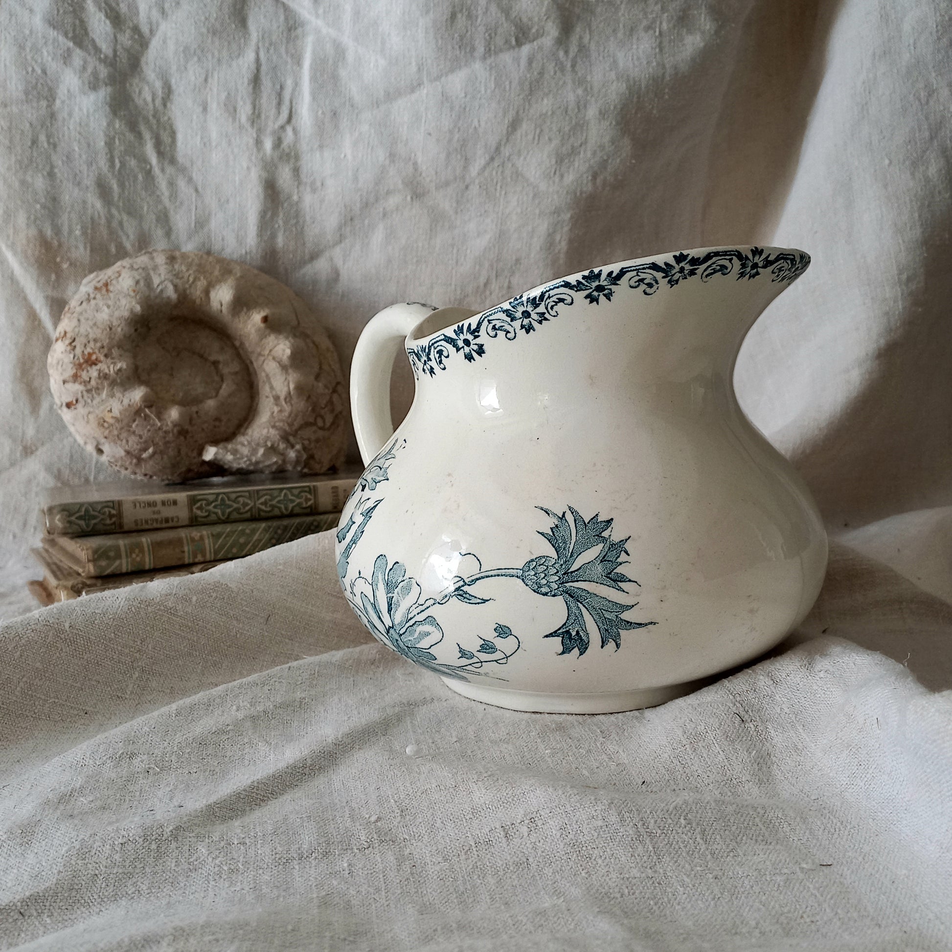 White ceramic pitcher with teal floral patterns on a textured fabric background