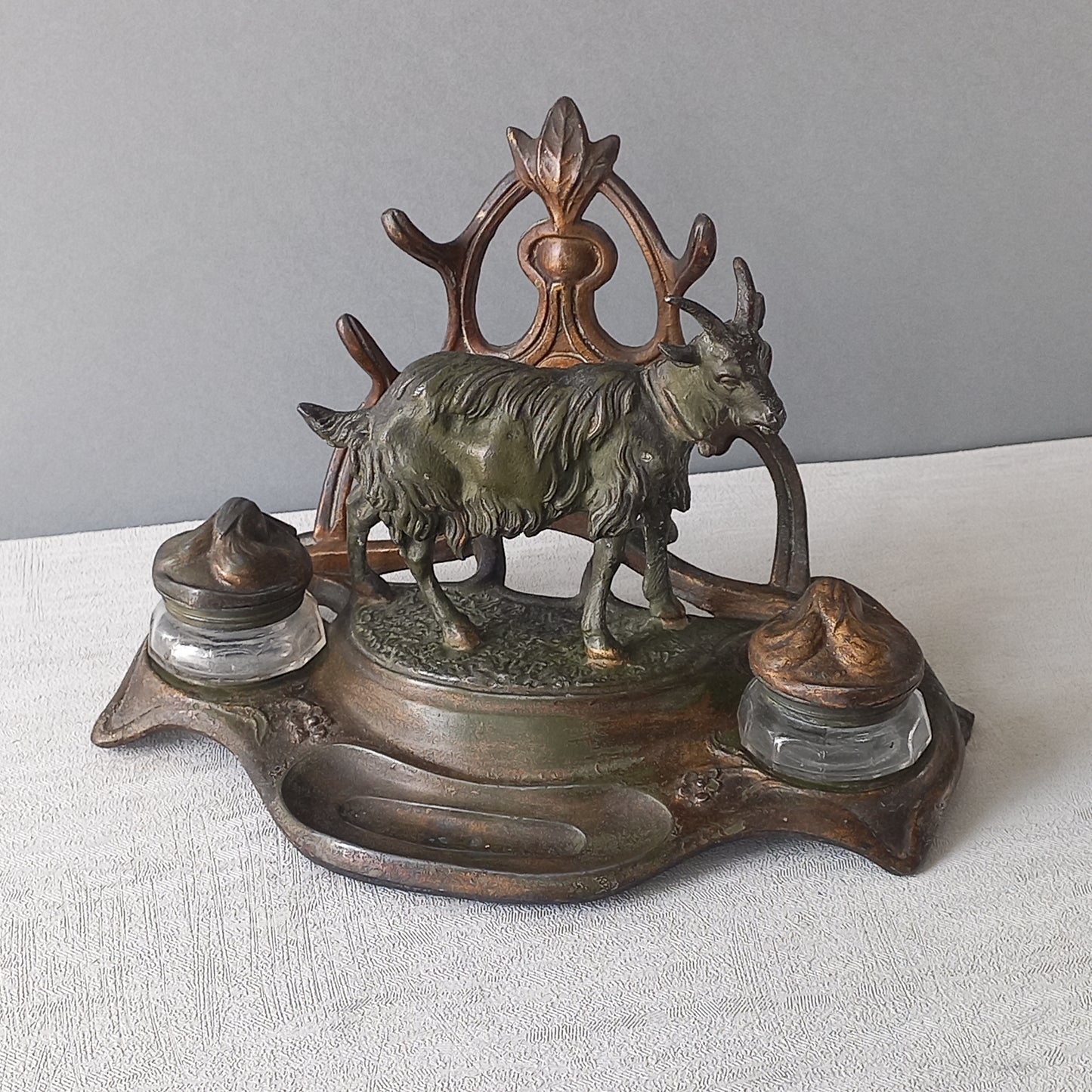 A stunning French art nouveau double inkwell with a goat figurine.
This wonderful antique inkwell has been sculpted in metal and signed by the artist (see photos). Behind the beautiful goat figurine are two pen rests and either side of the goat are two small glass ink pots with decorative metal lids.
The metal is finished in a lovely shade of green that has worn over time with traces of gold colour beneath - it has a wonderful patina of time all over it.