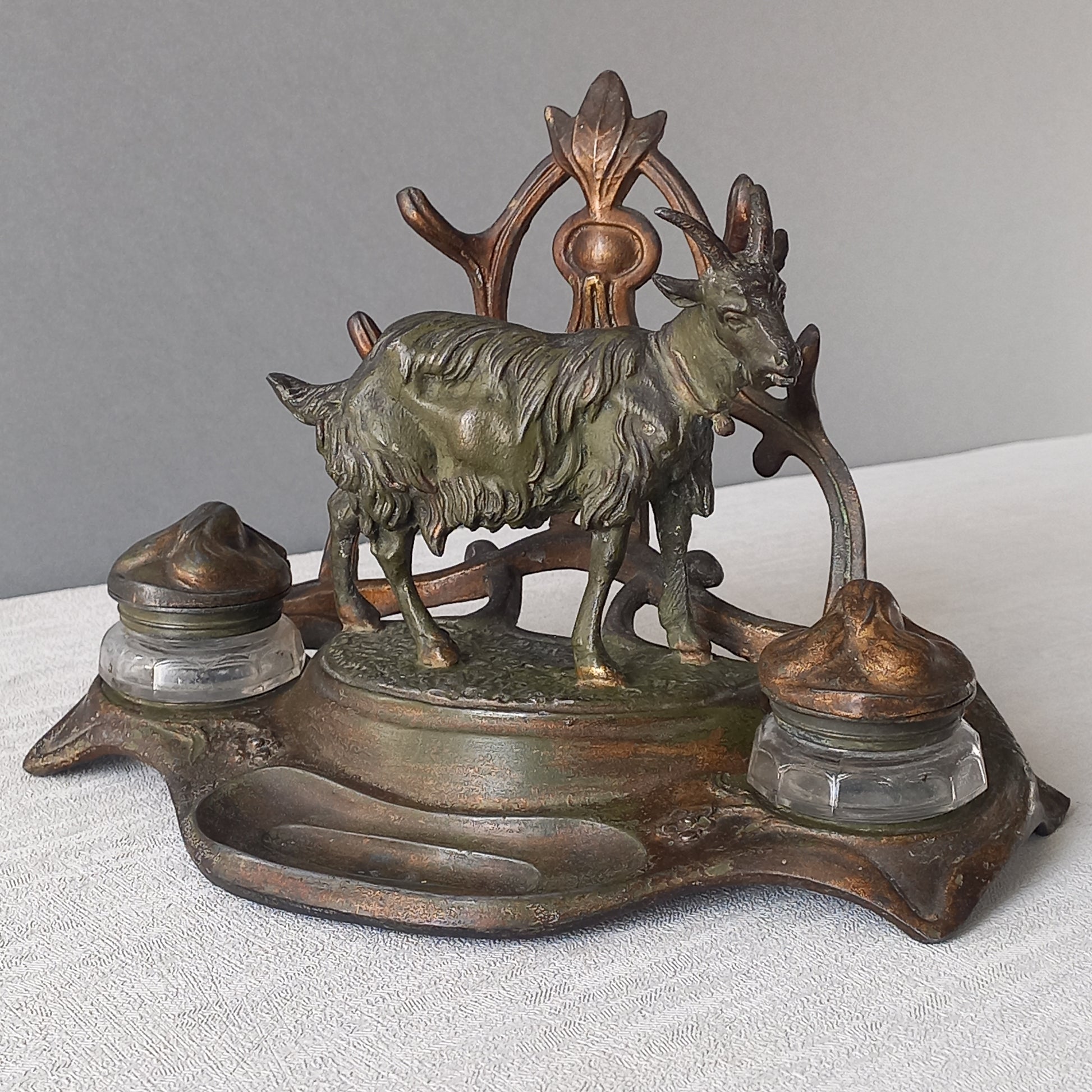 A stunning French art nouveau double inkwell with a goat figurine.
This wonderful antique inkwell has been sculpted in metal and signed by the artist (see photos). Behind the beautiful goat figurine are two pen rests and either side of the goat are two small glass ink pots with decorative metal lids.
The metal is finished in a lovely shade of green that has worn over time with traces of gold colour beneath - it has a wonderful patina of time all over it.