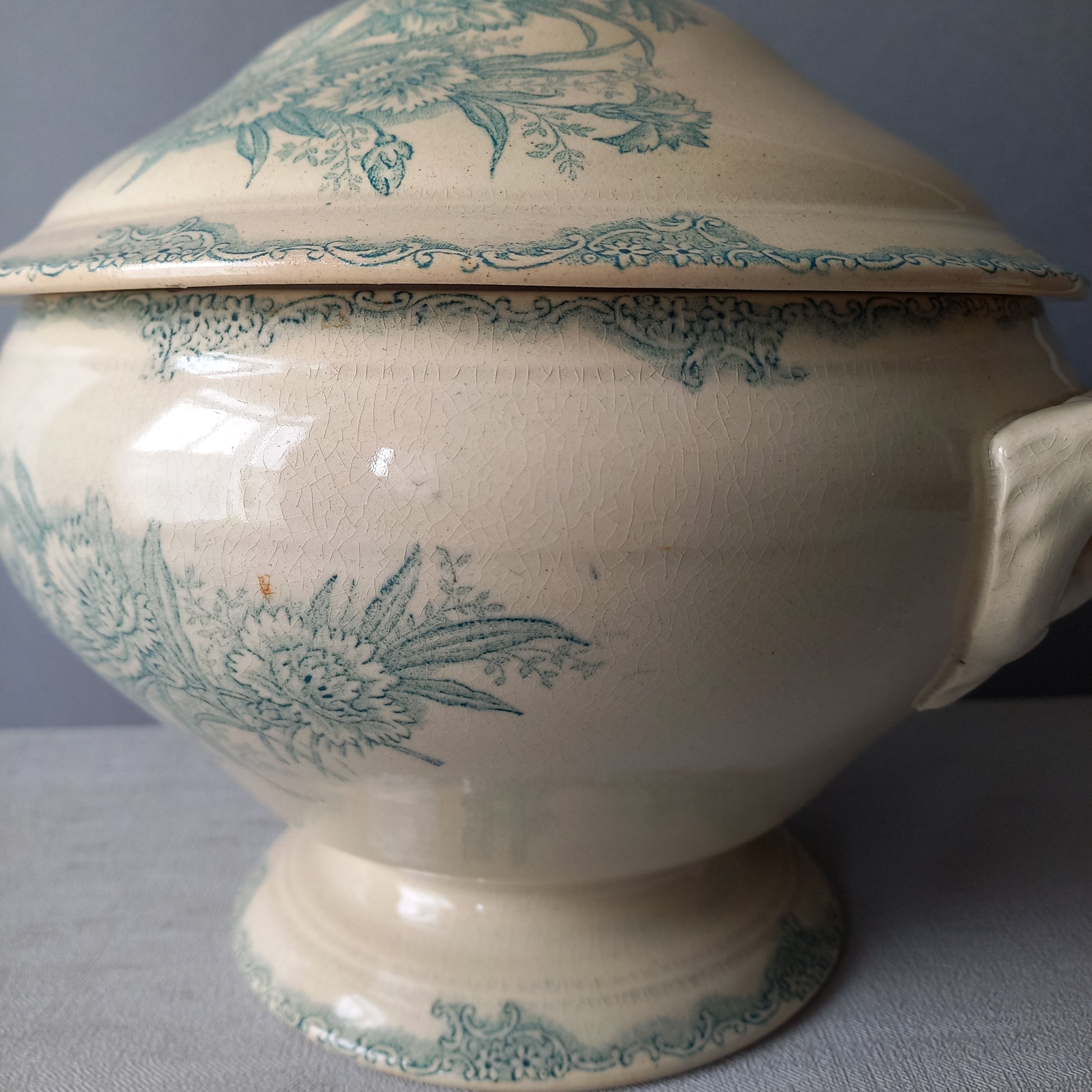 A pretty antique ironstone soup tureen with aged and faded floral transfer pattern in a beautiful shade of blue green or teal. Over time this wonderful old tureen has developed a pleasing faded creamy white finish. In summary, a beautiful piece of authentic antique ironstone from France.