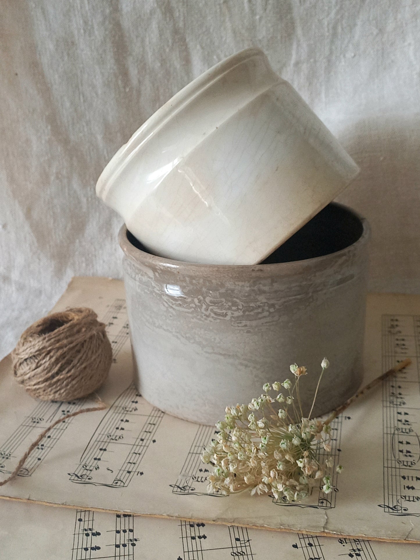 Two ceramic pots stacked on a surface with dried flowers and twine
