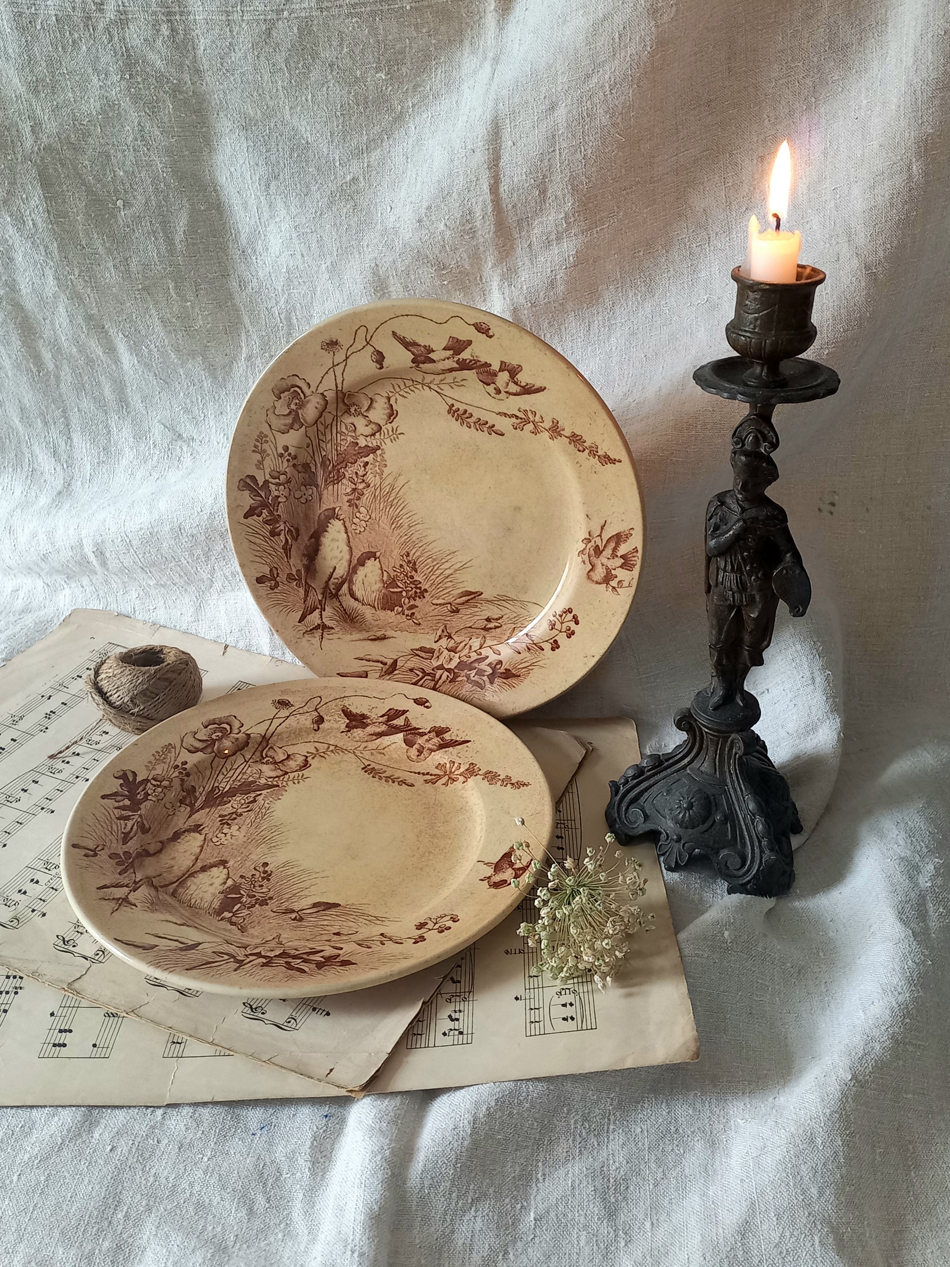 Two decorative antique plates with intricate designs on a white fabric background with a candle.