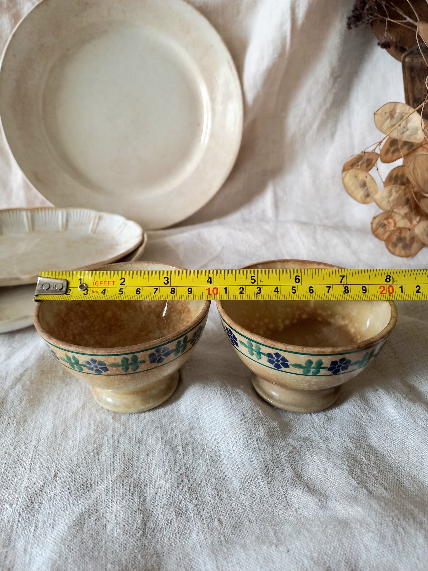 Two ceramic bowls with floral patterns on a white cloth, measured with a tape measure.