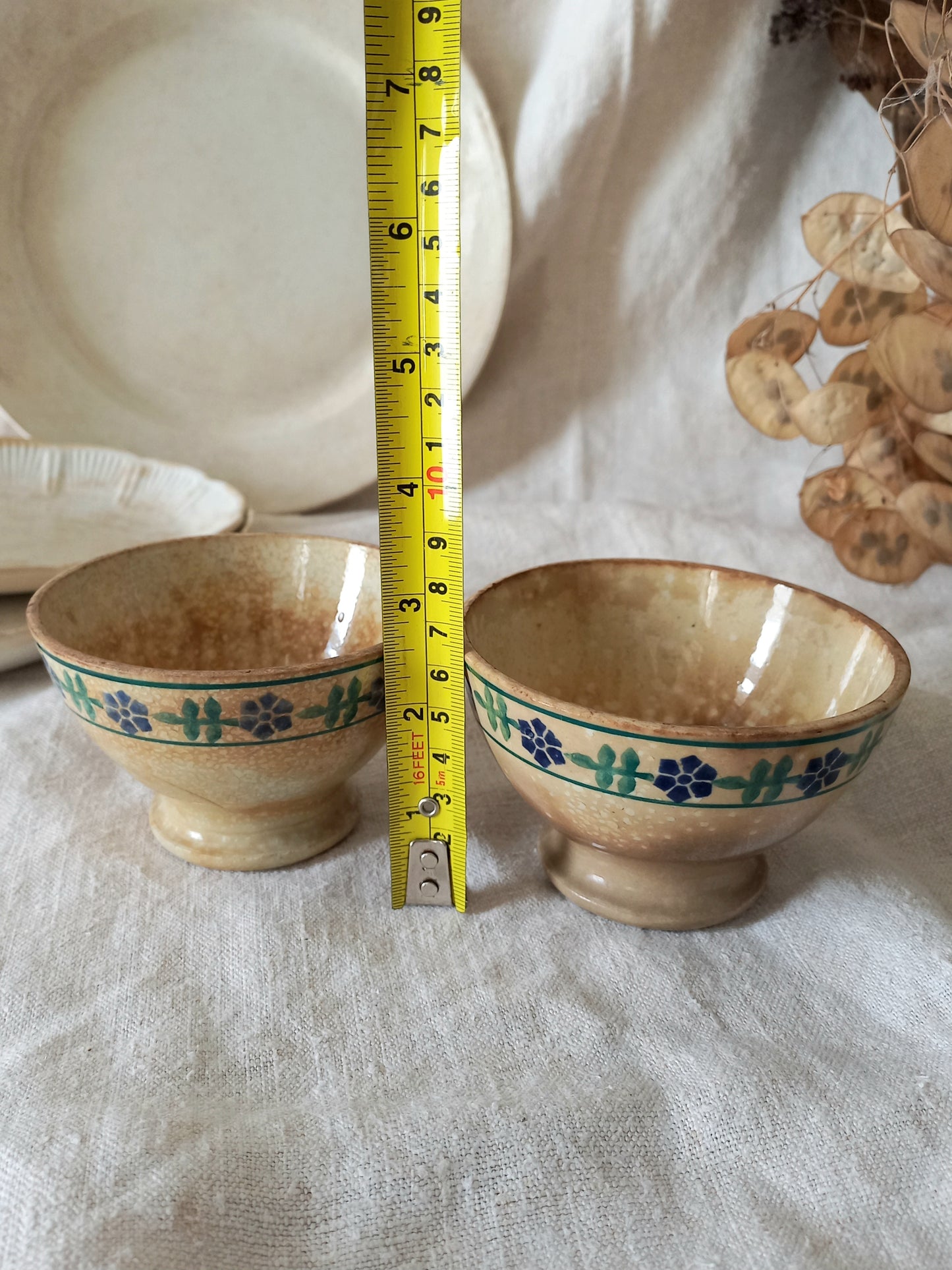 Two ceramic bowls with floral patterns on a textured surface, measured by a tape measure.