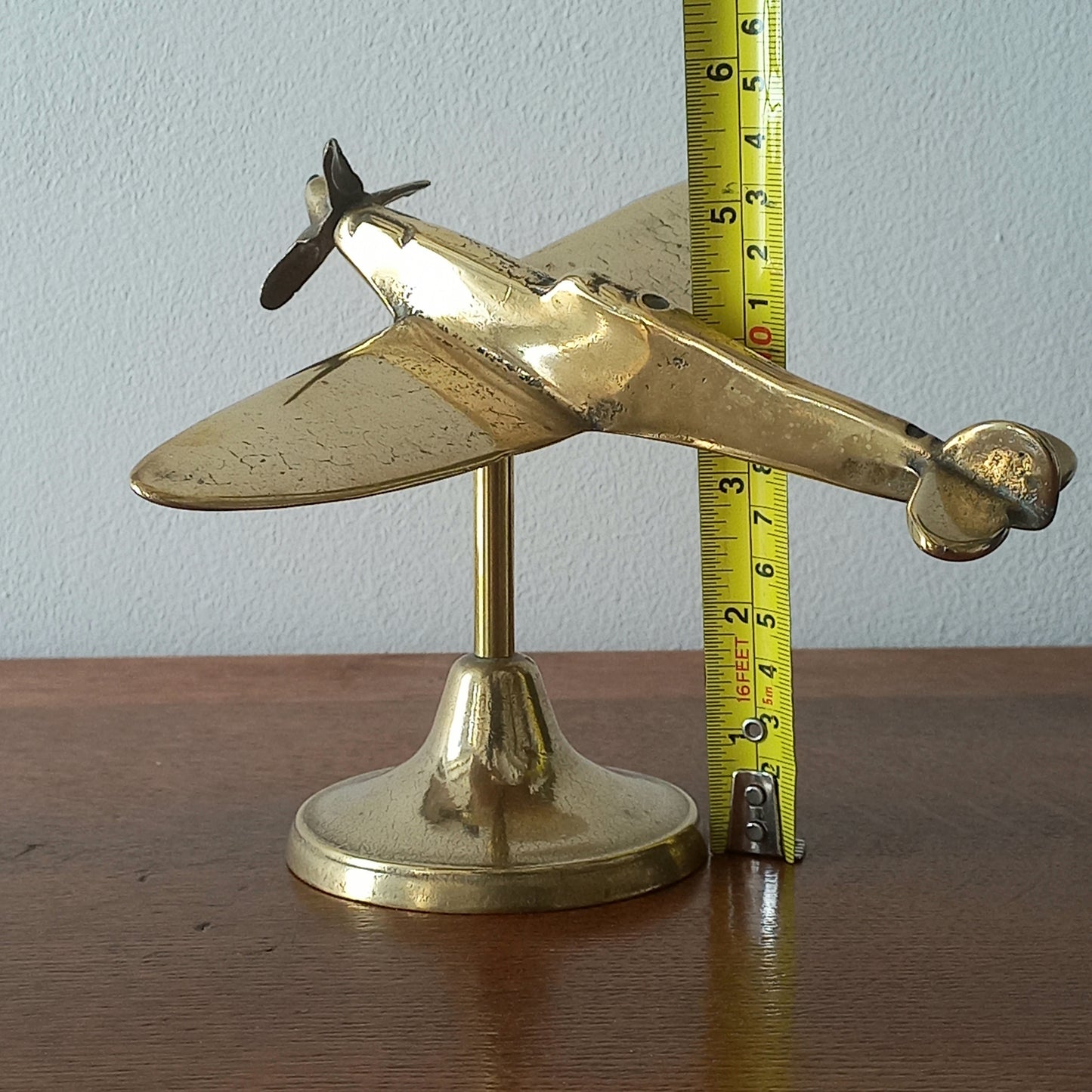 Brass airplane model with a measuring tape for scale on a wooden surface.