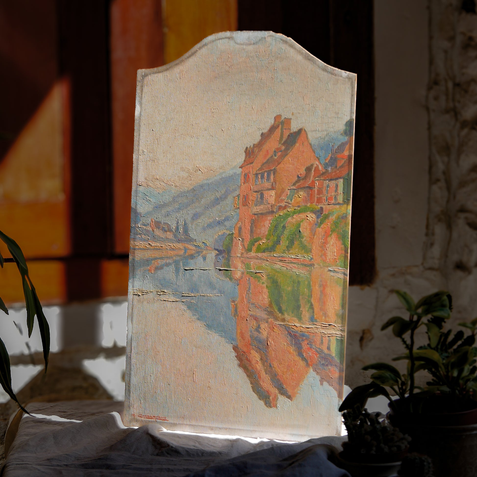 An original vintage oil painting depicting a village on the banks of a large river. It looks similar to the Rhine River Danube in Germany, and with the large hills/mountains in the background maybe the Black Forest, although it could be many places in Europe and perhaps even in France where we purchased this wonderful piece of original art on wooden board.