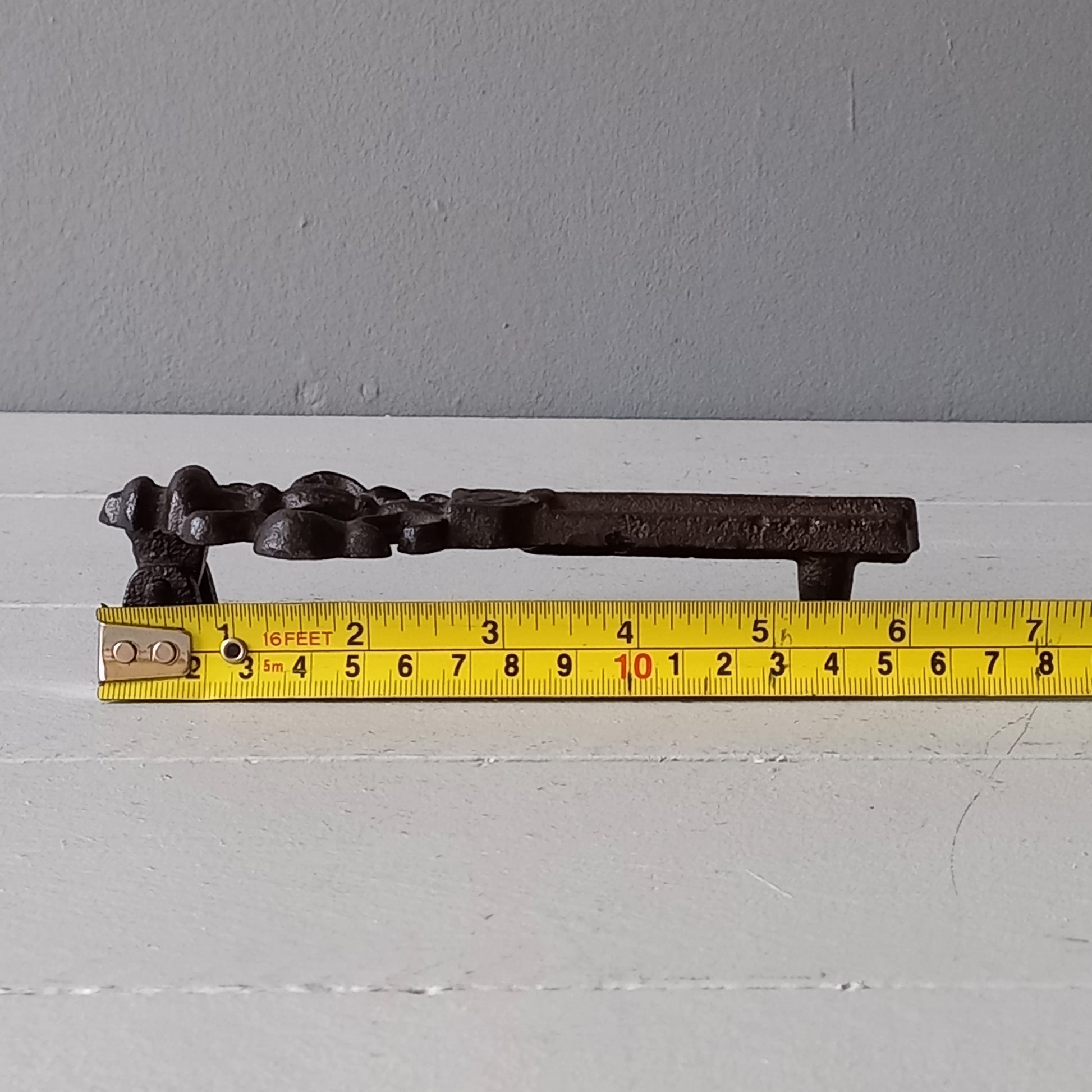 Decorative metal handle on a door with a tape measure for scale.