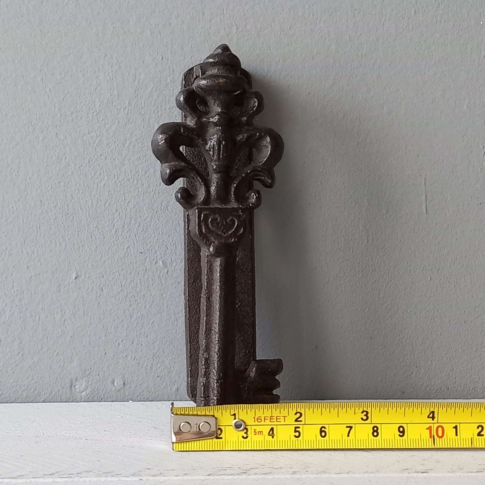 Decorative metal bracket with a measuring tape for scale on a gray background