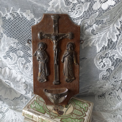 Wall-mounted vintage/antique religious wall decor with metal crucifix and religious figures, and a glass Holy Water font mounted to a wooden base. A great piece of original religious decor from France.
