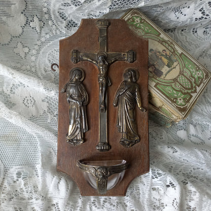 Wall-mounted vintage/antique religious wall decor with metal crucifix and religious figures, and a glass Holy Water font mounted to a wooden base. A great piece of original religious decor from France.