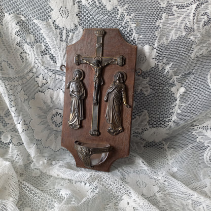 Wall-mounted vintage/antique religious wall decor with metal crucifix and religious figures, and a glass Holy Water font mounted to a wooden base. A great piece of original religious decor from France.