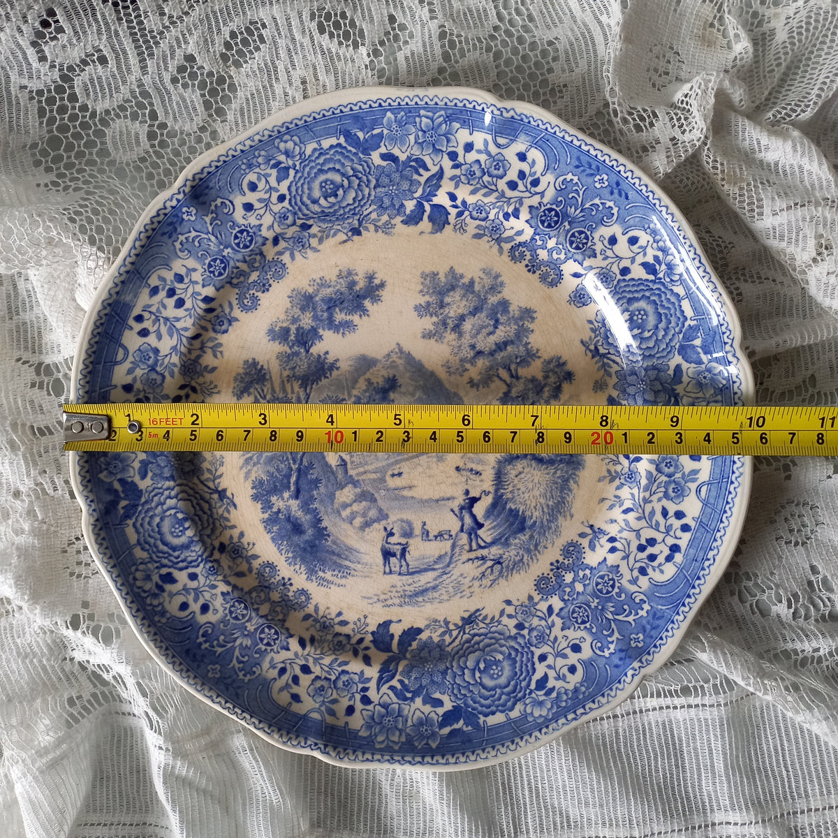Blue and white decorative plate with a ruler for scale on a lace background