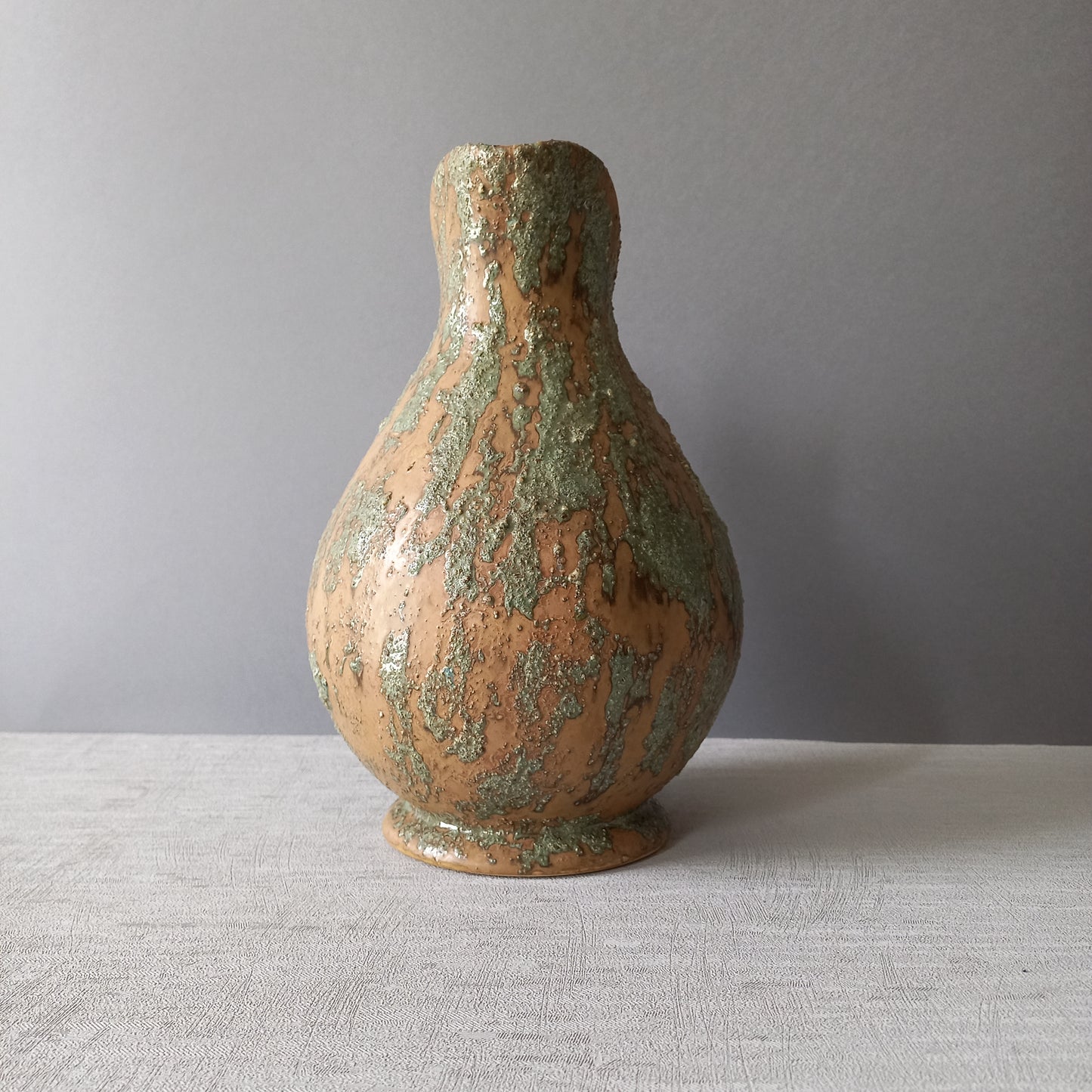 Vintage pottery pitcher or jug with earthy tones and green pattern in relief