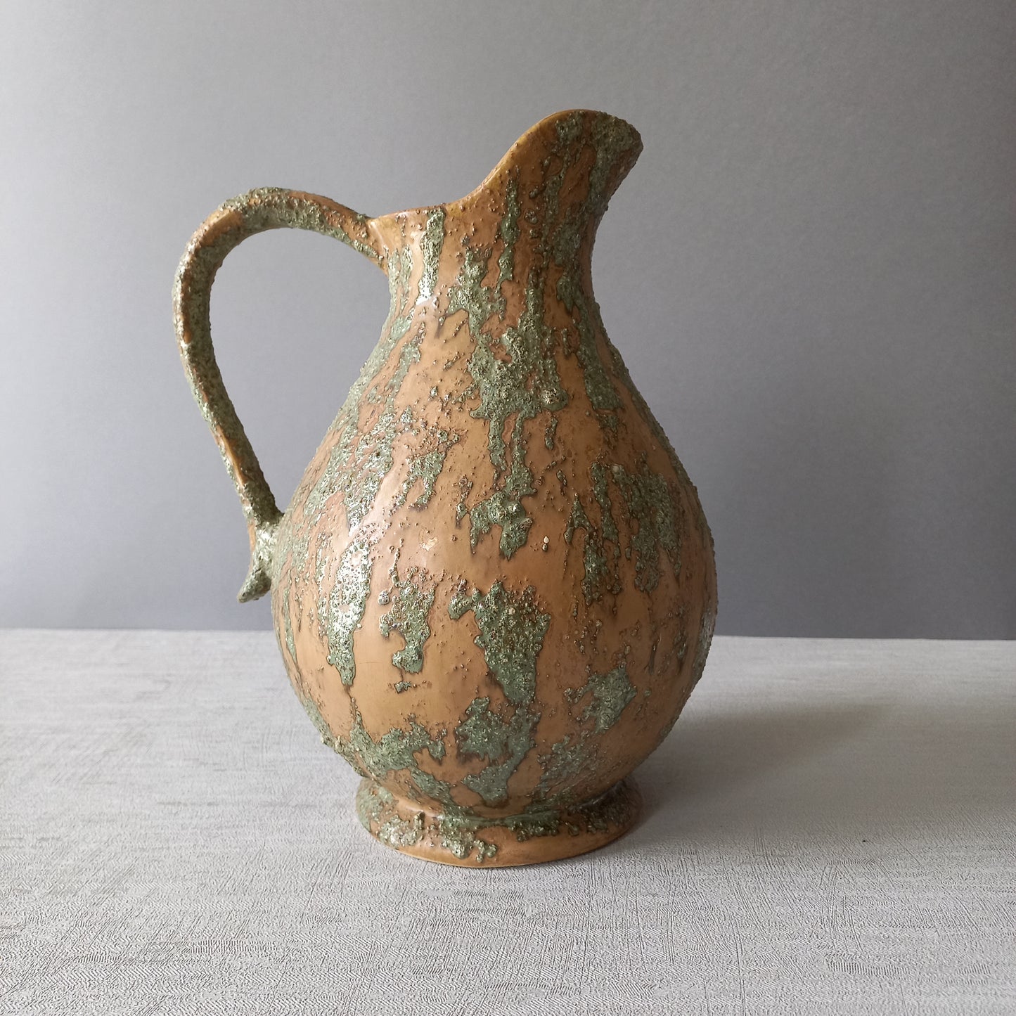 Vintage pottery pitcher or jug with earthy tones and green pattern in relief