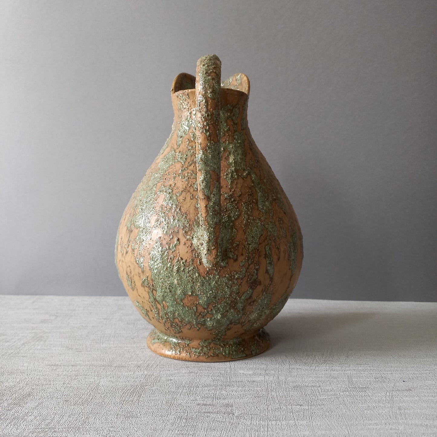 Vintage pottery pitcher or jug with earthy tones and green pattern in relief