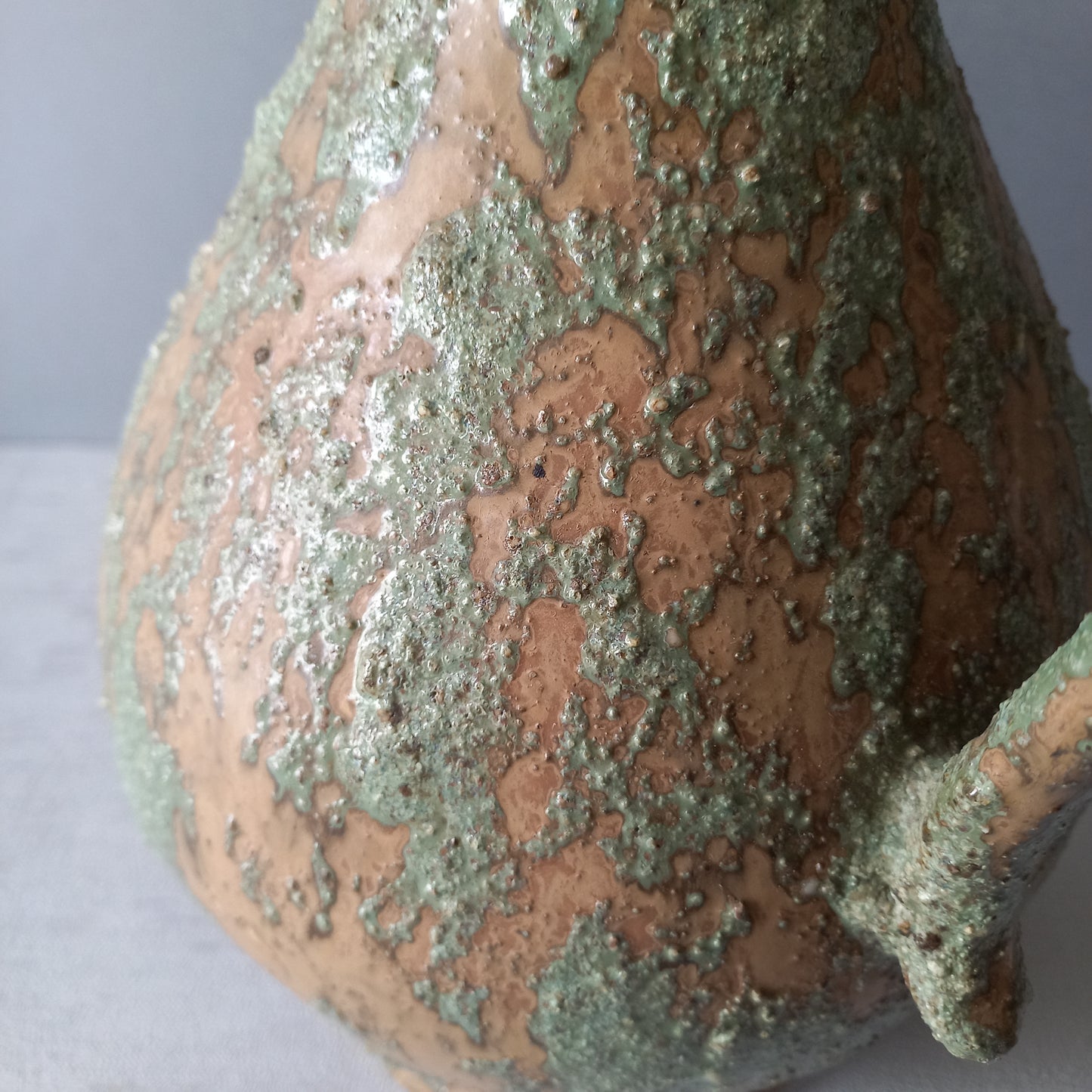 Vintage pottery pitcher or jug with earthy tones and green pattern in relief