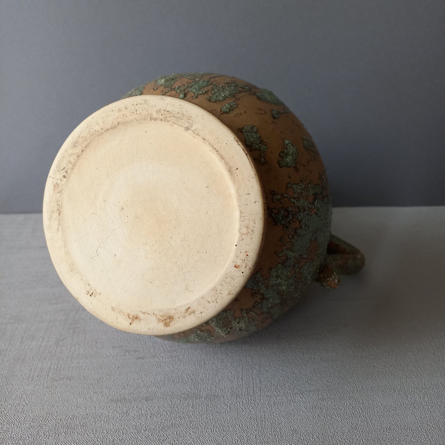 Vintage pottery pitcher or jug with earthy tones and green pattern in relief