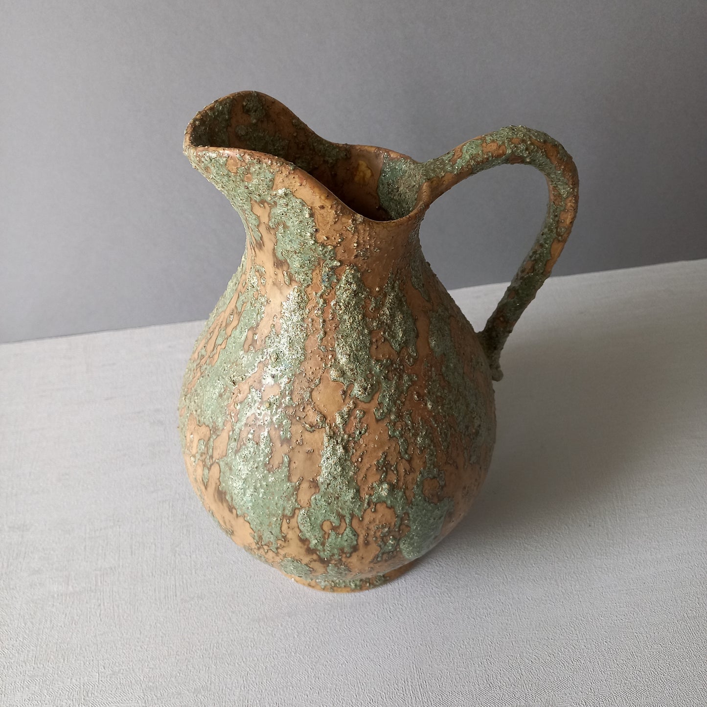 Vintage pottery pitcher or jug with earthy tones and green pattern in relief