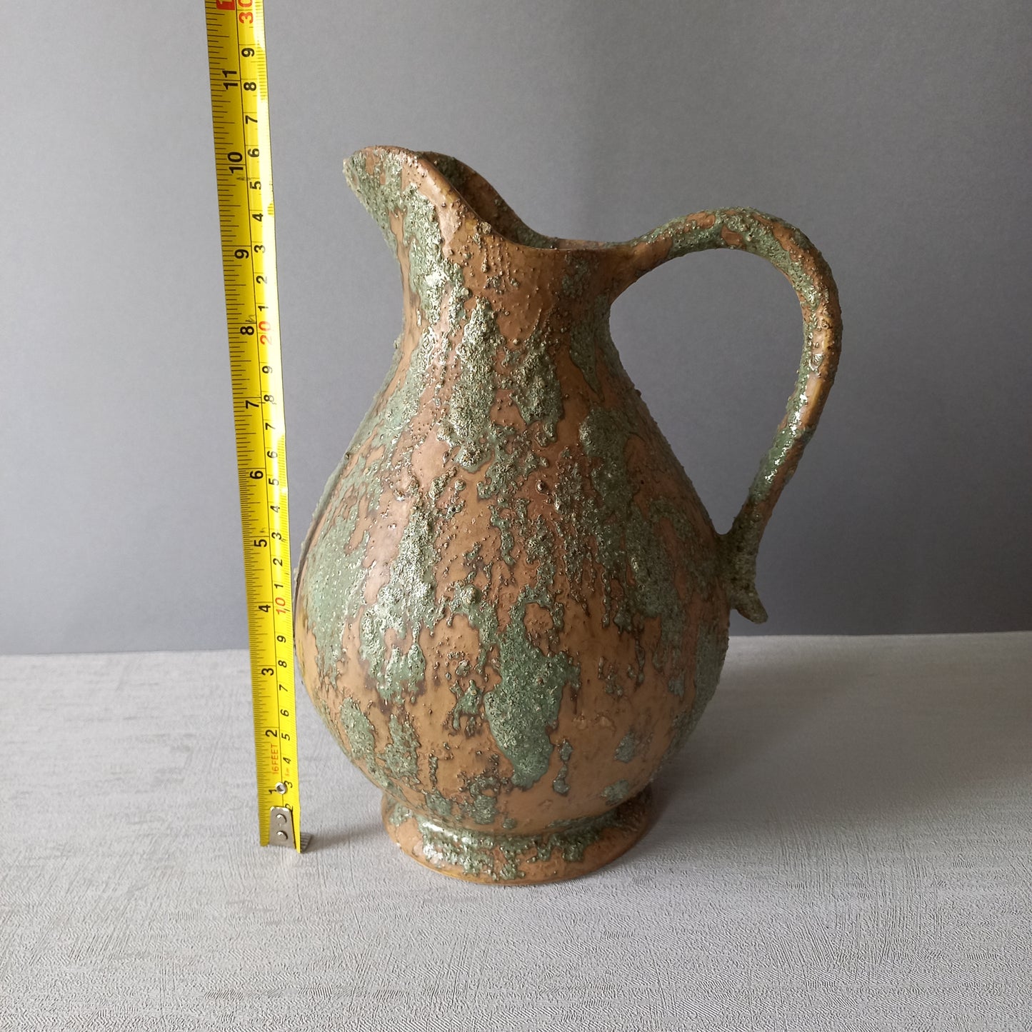 Vintage pottery pitcher or jug with earthy tones and green pattern in relief