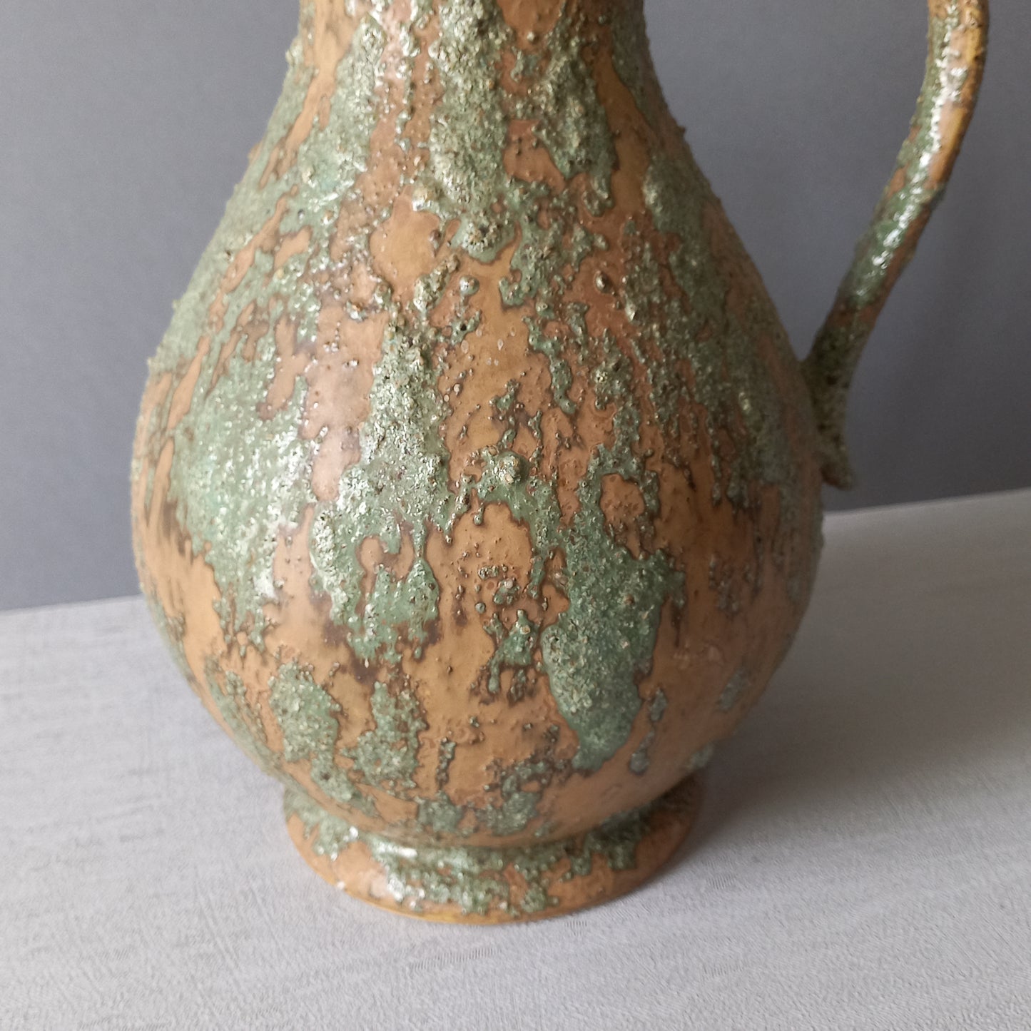 Vintage pottery pitcher or jug with earthy tones and green pattern in relief