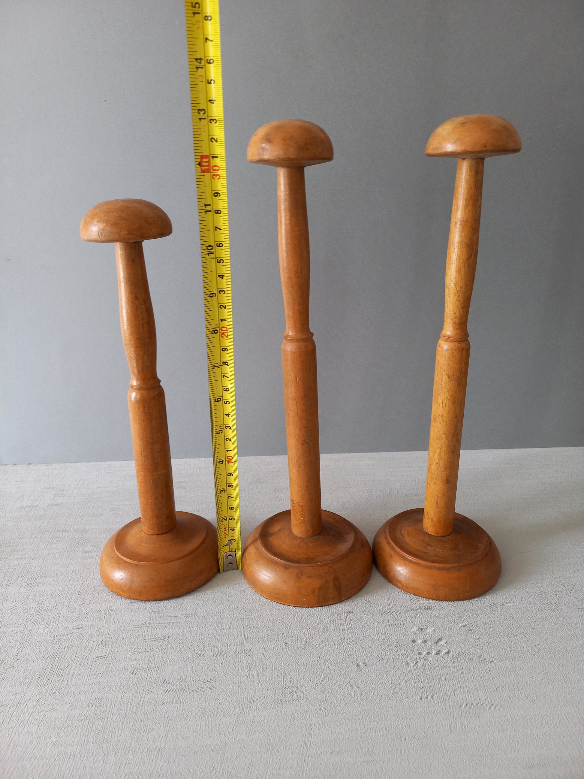 Three vintage wooden hat stands of different sizes on a gray background with a measuring tape for scale.