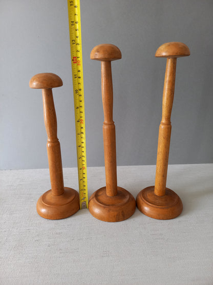 Three vintage wooden hat stands of different sizes on a gray background with a measuring tape for scale.