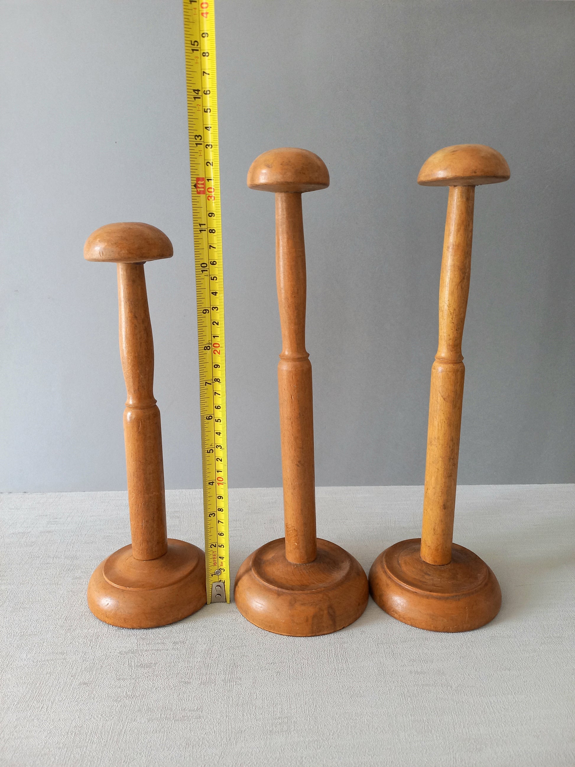 Three vintage wooden hat stands of different sizes on a gray background with a measuring tape for scale.