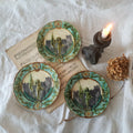 Three decorative plates with artistic designs on a textured surface with a candle and dried flower.