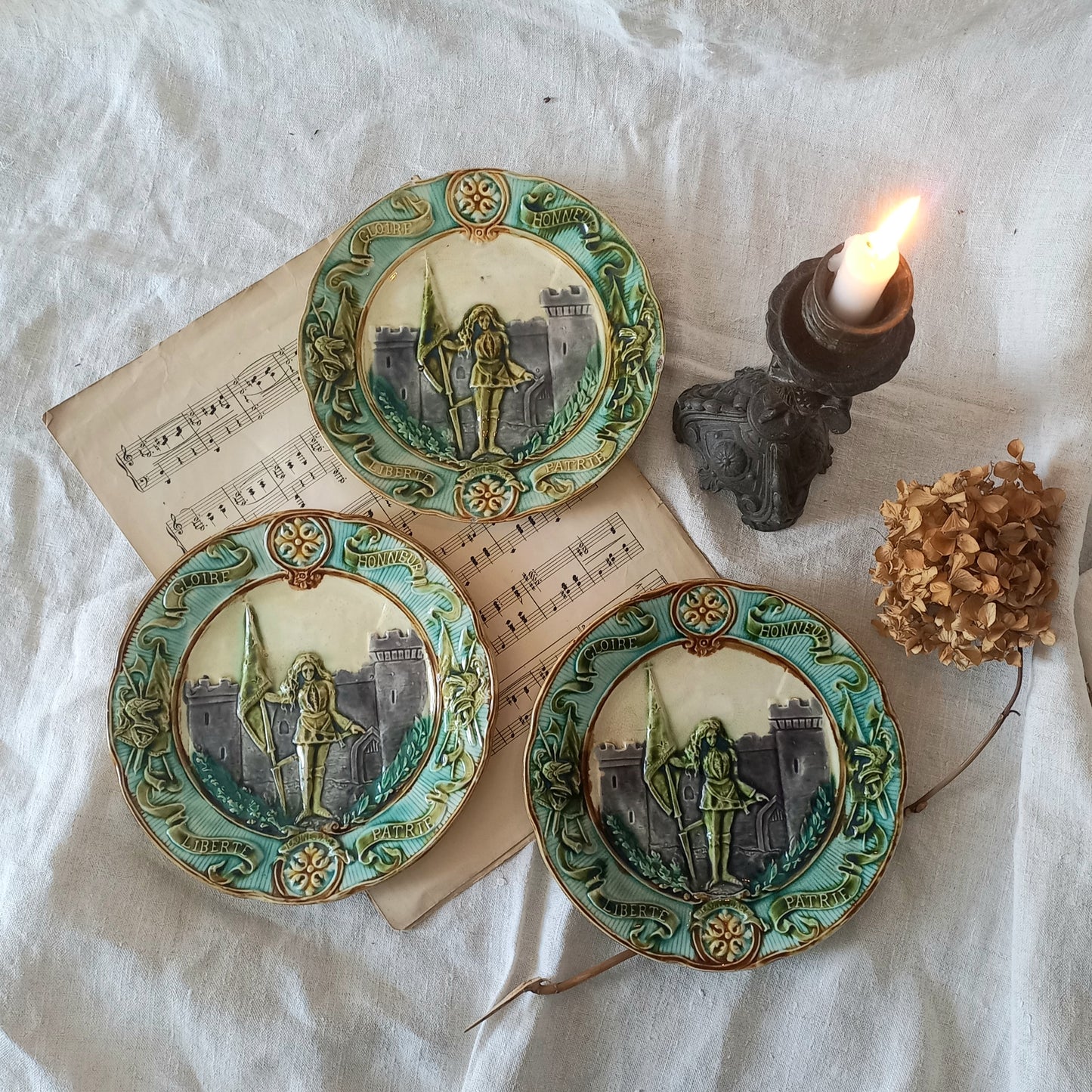 Three decorative plates with artistic designs on a textured surface with a candle and dried flower.