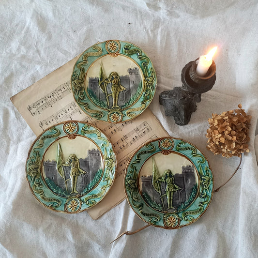 Three decorative plates with artistic designs on a textured surface with a candle and dried flower.