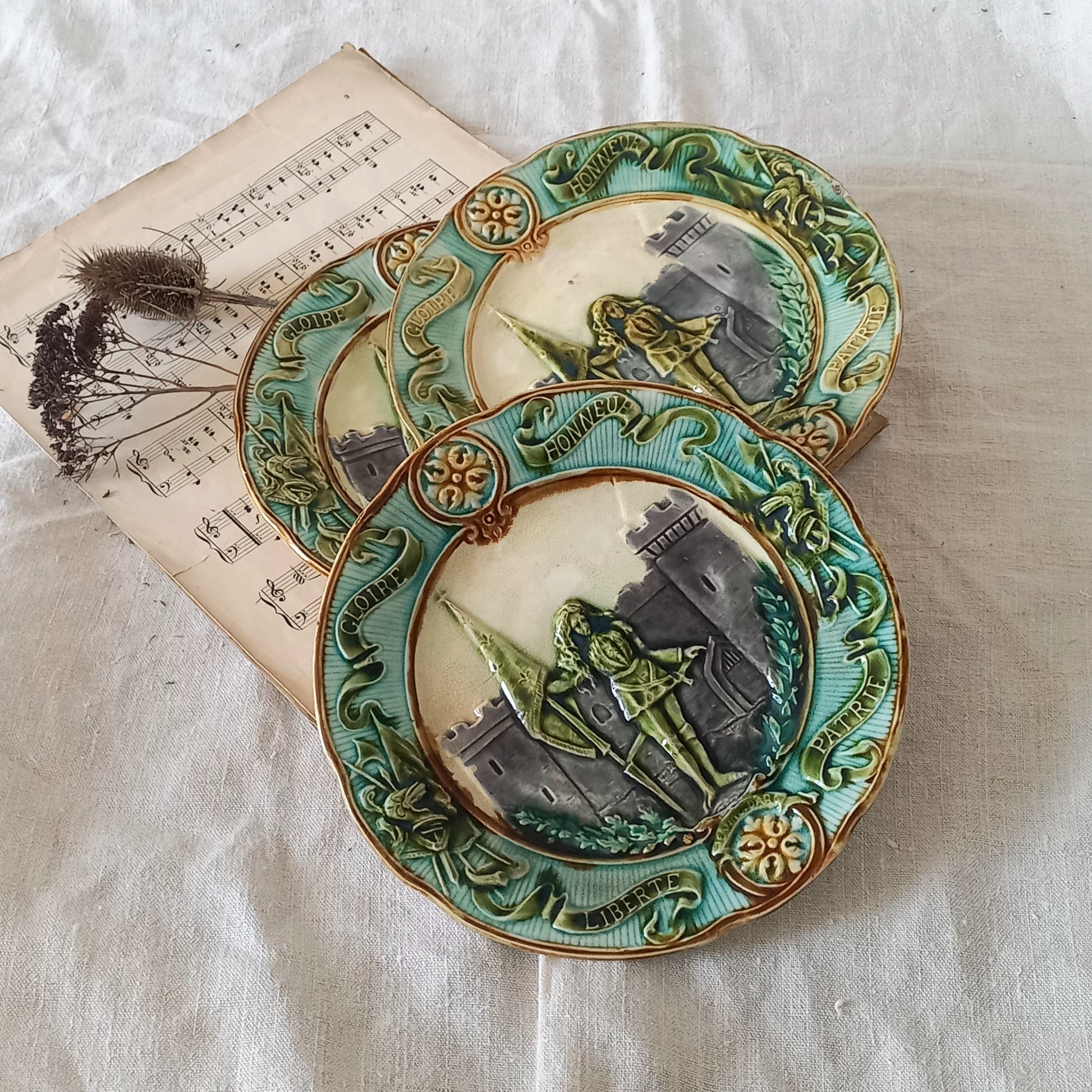 Three decorative plates with embossed designs on a textured surface with an old book and dried plants.
