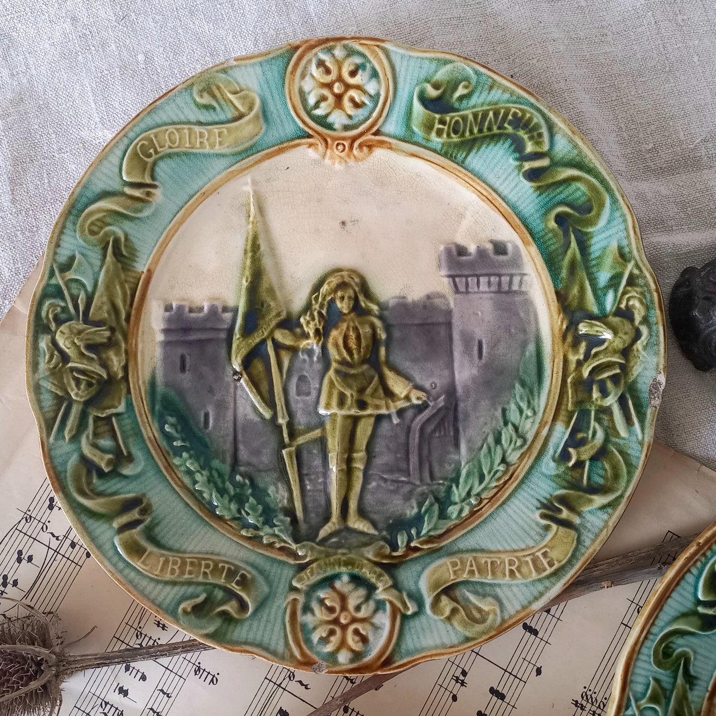 Decorative plate with a central figure holding a spear, surrounded by decorative elements and text.