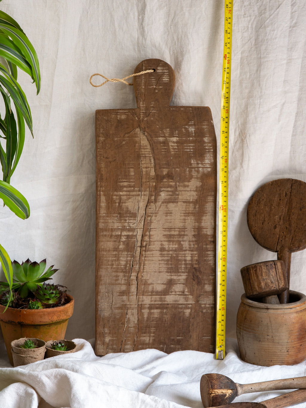 A large vintage wooden chopping board from south west France, shaped by years of use and hand-worn edges. Its rough texture and deep patina tell the story of daily bread, shared meals, and time well lived.