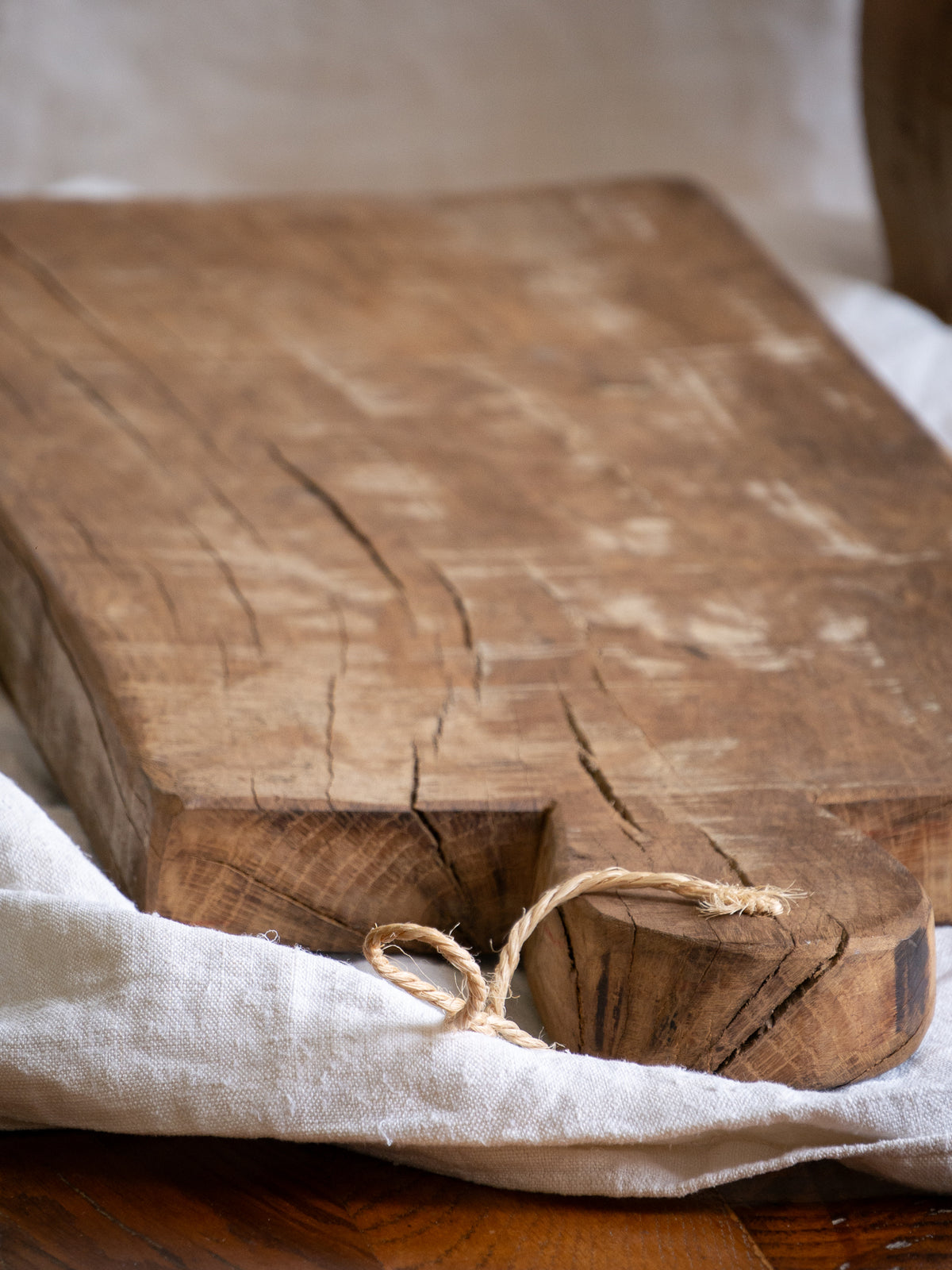 A large vintage wooden chopping board from south west France, shaped by years of use and hand-worn edges. Its rough texture and deep patina tell the story of daily bread, shared meals, and time well lived.