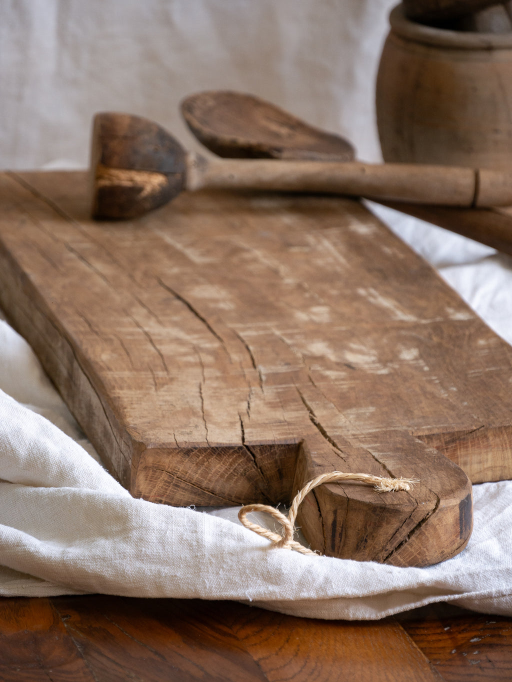 A large vintage wooden chopping board from south west France, shaped by years of use and hand-worn edges. Its rough texture and deep patina tell the story of daily bread, shared meals, and time well lived.