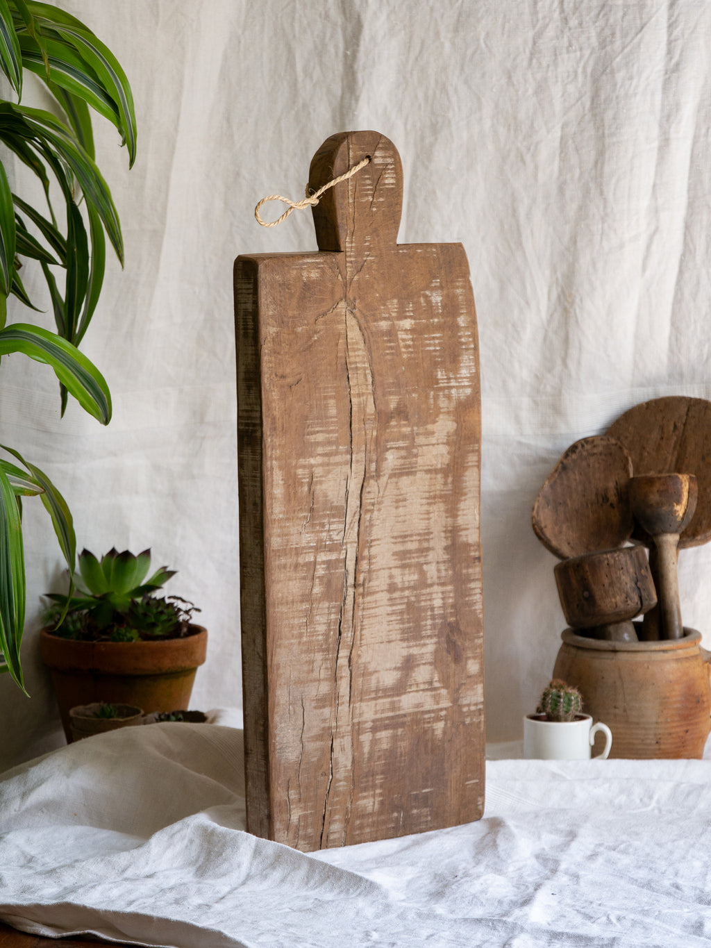 A large vintage wooden chopping board from south west France, shaped by years of use and hand-worn edges. Its rough texture and deep patina tell the story of daily bread, shared meals, and time well lived.